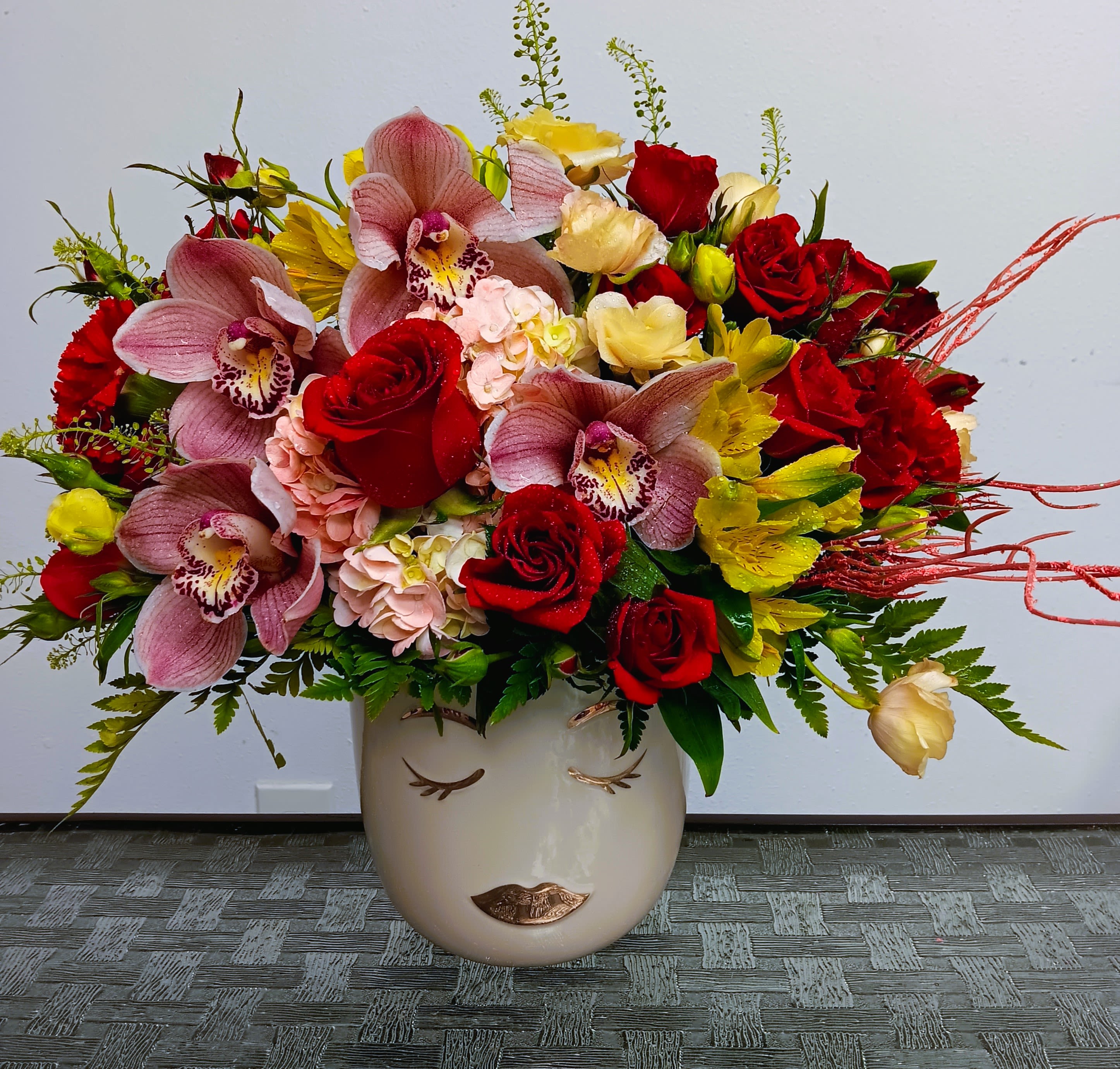 Mixed bouquet of red roses, pink orchids, and yellow flowers in a face vase
