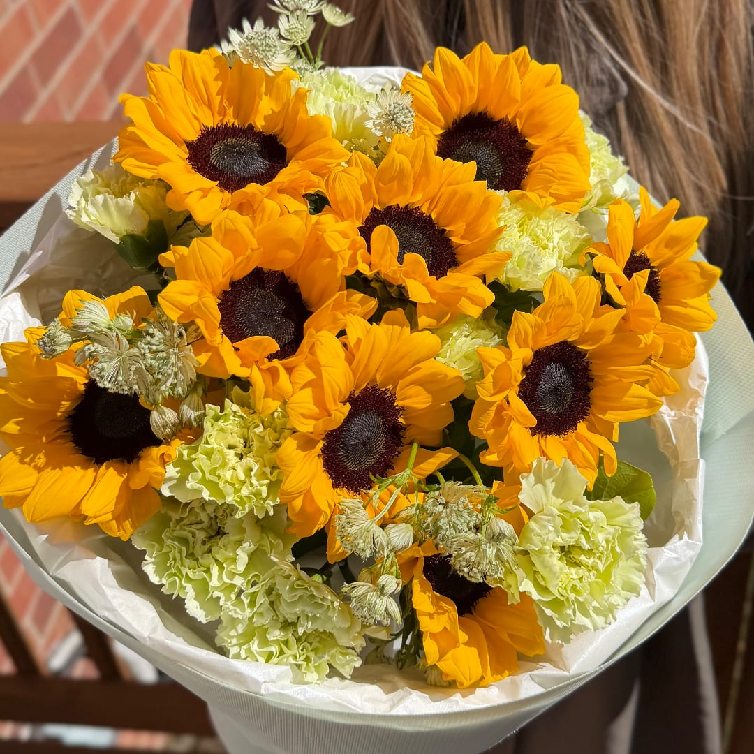 Bouquet of sunflowers and pale green carnations wrapped in white paper