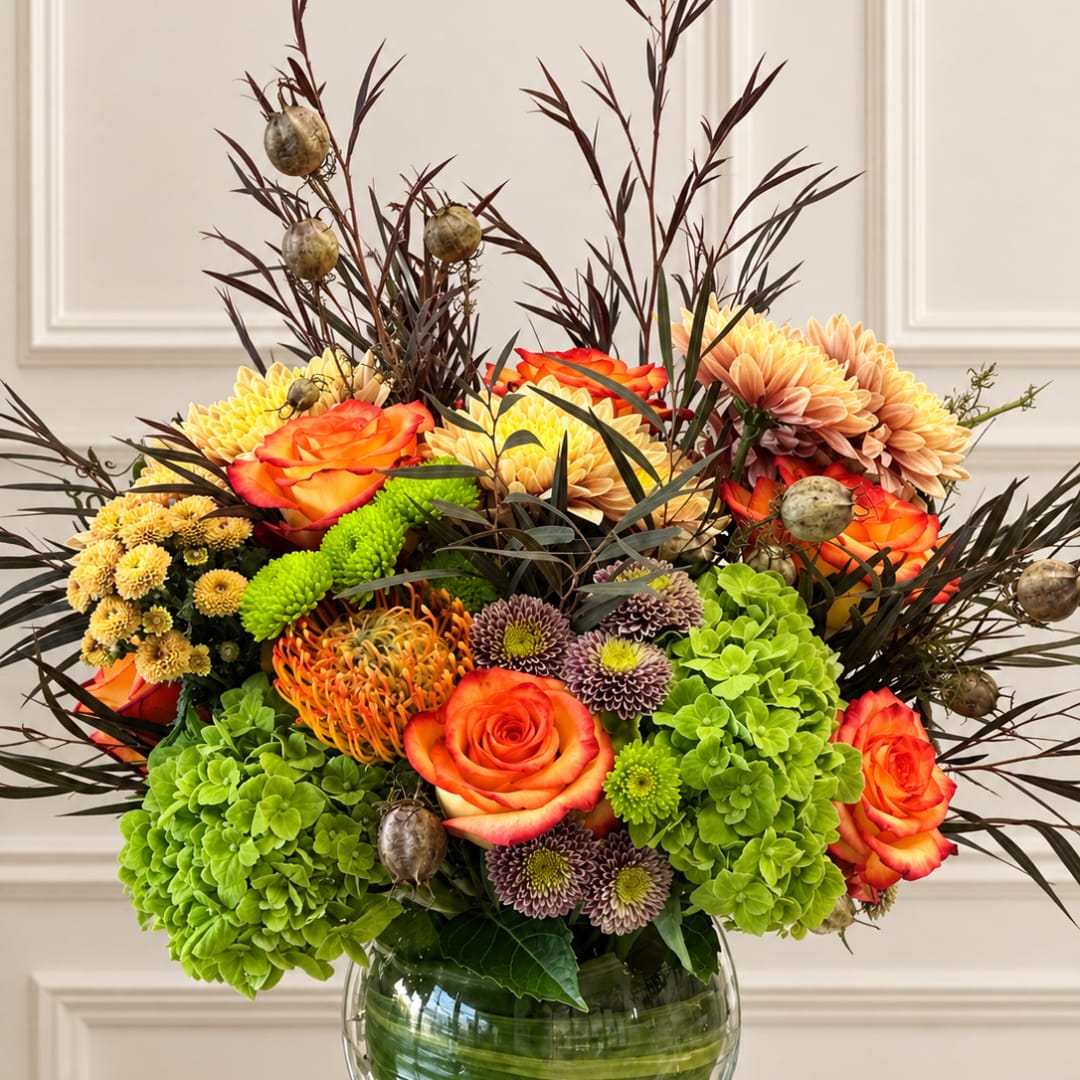 Mixed bouquet of orange roses, chrysanthemums, and green hydrangeas in a glass vase