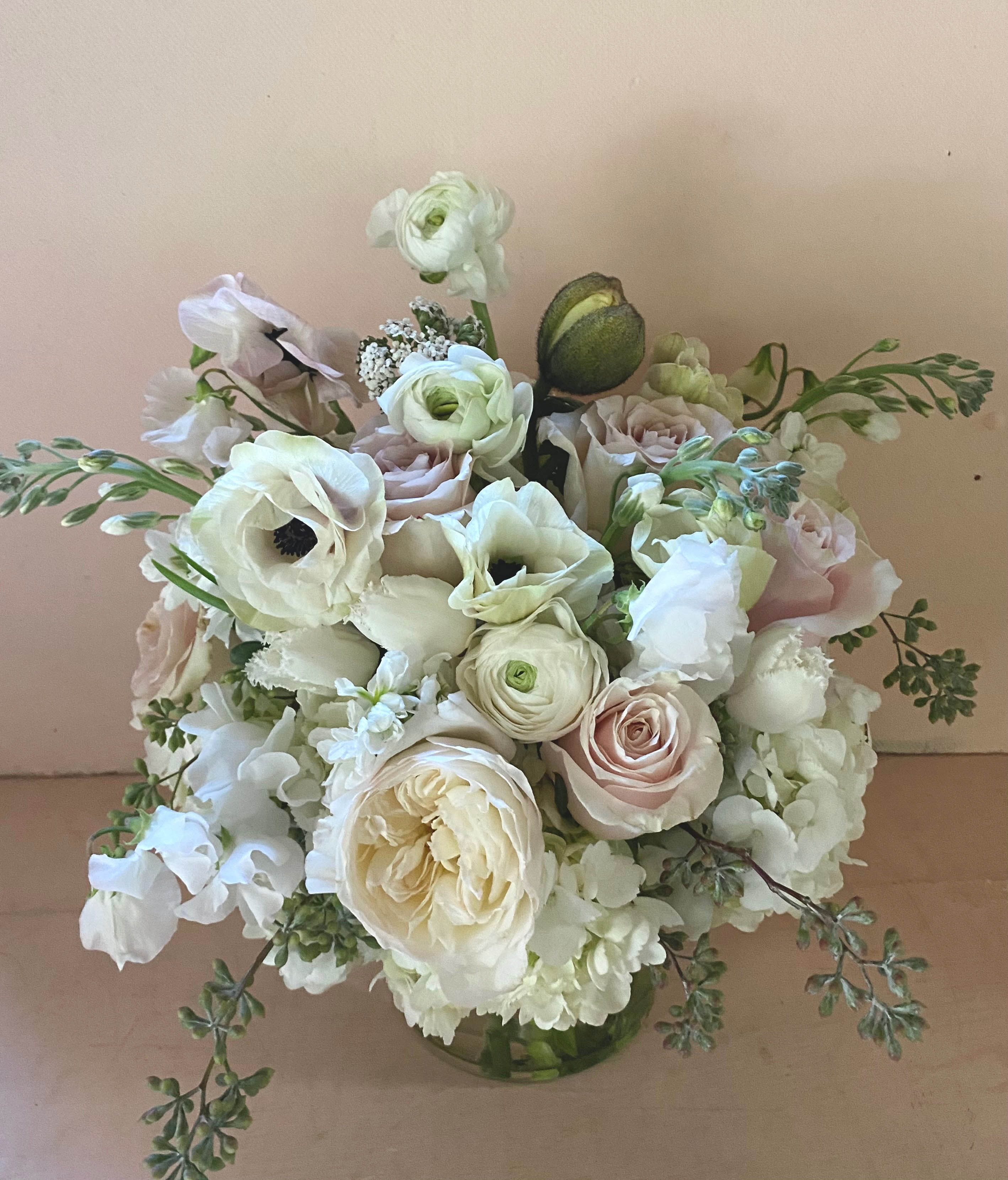 Winnie White arrangement - The white and wonderful stems in this beautiful arrangement create a floral bliss of light and soothing energy. Perfect for the sympathy wishes, the memorial service or for the recipient living with a pale palette at home. A natural and pretty selection of seasonal stems arrangemed beautifully in a 5' by 7' clear cylinder vase, a slim tall vase measurin appx 11" by 12". Choose the deluxe for more flowers appx 11" by 13"  or the premium for even more flowers and a fuller arrangement appx 13" by 15"