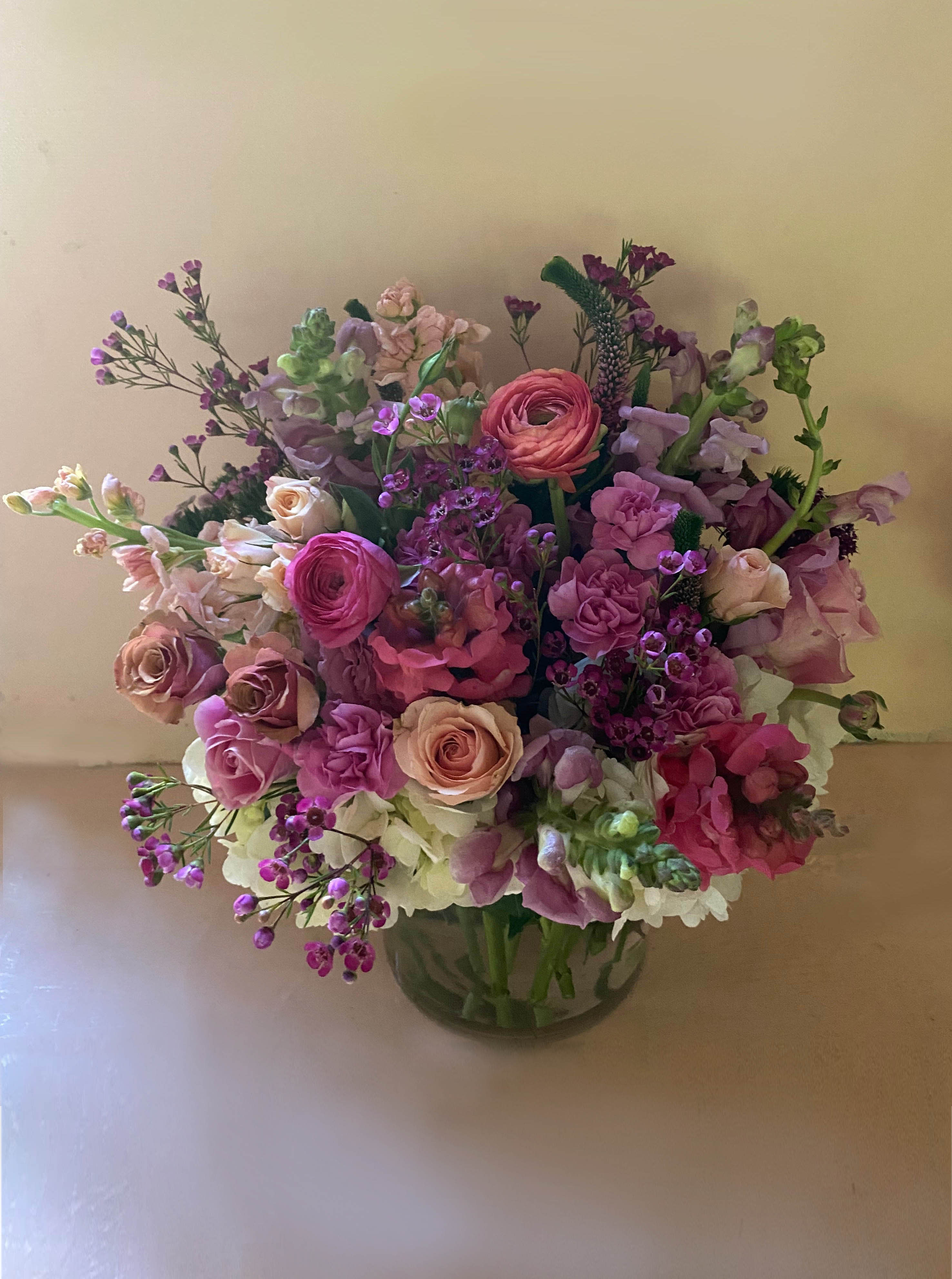 Lorelei Arrangement - Gorgeous pink, purple and lavender palettte in this large and vibrant floral creation, arranged in a 6" by 6" clear cylinder vase of fresh, seasonal stems such as stock, roses, snapdragons, ranuncules etc. A bright light to a recipient who loves colors or needs cheering up. Choose the Deluxe for more stems or Premium for a fuller arrangement with more stems.