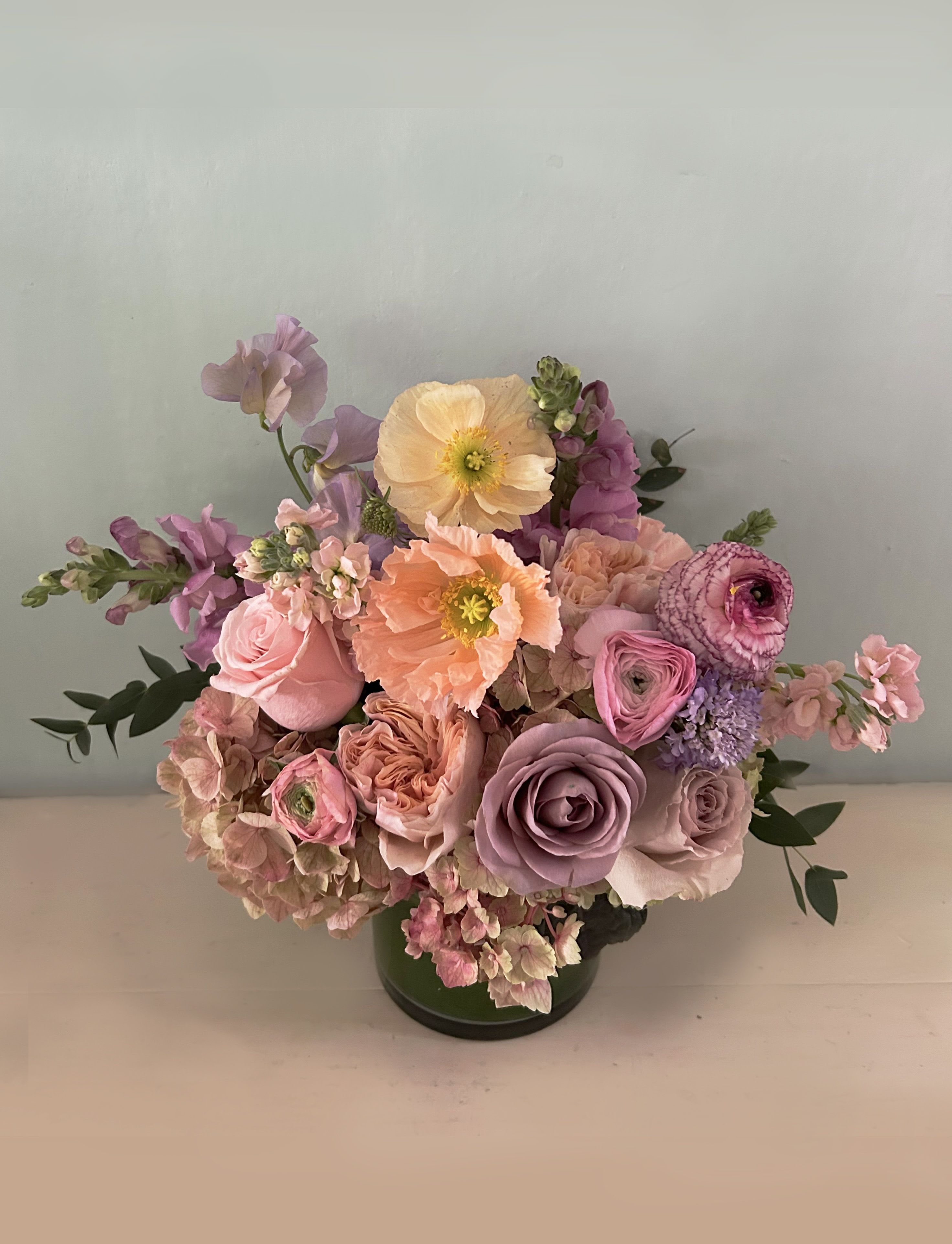 The Luna Love  - This gorgeous arrangement is small but has all the prettiest of colors in the world of dusty pastels. Lavender, ligth brown/purple, golden, coral stems of fresh seasonal beauty placed in a clear 4' by 4" glass vase with a bit of dusty greens - so cute for the office desk, the night stand or as a perfect gift of love an appreciation. Poppies and/or ranunculus, dahlias and/or other seasonal flowers make this arrangement perfect for most occasions.  Blomst LA only uses fresh, high quality flowers, all carefully selected every day to fit your flower order. Choose Deluxe for a fuller and larger arrangement with more flowers. Choose premium for the even larger version of the arrangement with even more flowers. We offer a personal hand delivery by our own delivery staff and guarantee the flowers will look perfect, when they arrive. 