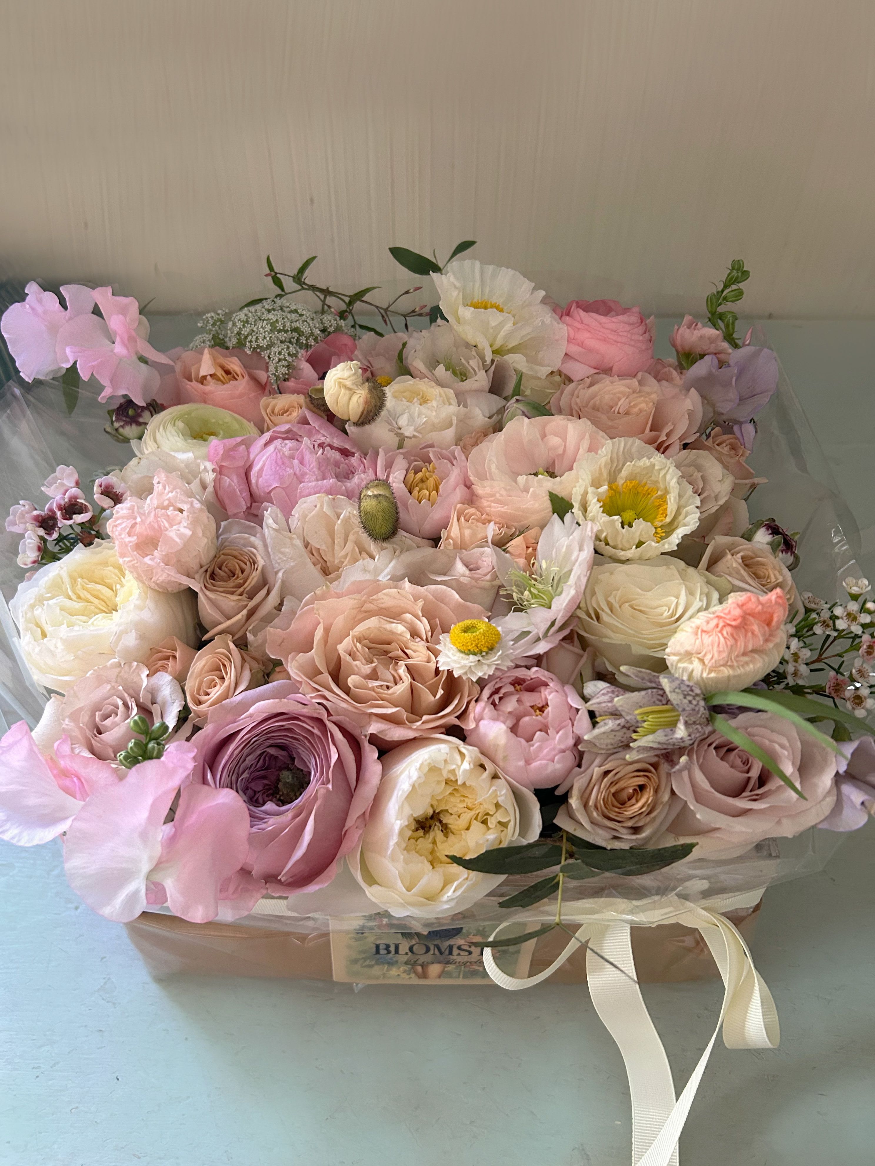 Golden Light Flower box - Beautiful blooming signature Blomst flower box full of fresh flowers in a nude, white and pale pastel palette with little hints of yellow. Perfect as a gift of romance or just a "Thank you", "I'm sorry" or "Happy Birthday".  The box is made in natural light wood, is 8" by 8 inches" and 4" tall. You can upgrade to Deluxe for more luxurious flowers and to premium for a larger box, 14" by 14" filled with the most gorgeous flowers. We wrap in silk paper and use beautiful ribbon, pretty wrapping details for that beautiful impact at delivery. Blomst LA only uses fresh, high quality flowers, all carefully selected every day to fit your flower order. We offer a personal hand delivery by our own delivery staff and guarantee the flowers will look perfect, when they arrive. We deliver in Glendale, Pasadena, Eagle Rock, Hollywood, Burbank, Beverly Hills - and everywhere else in Greater Los Angeles. 