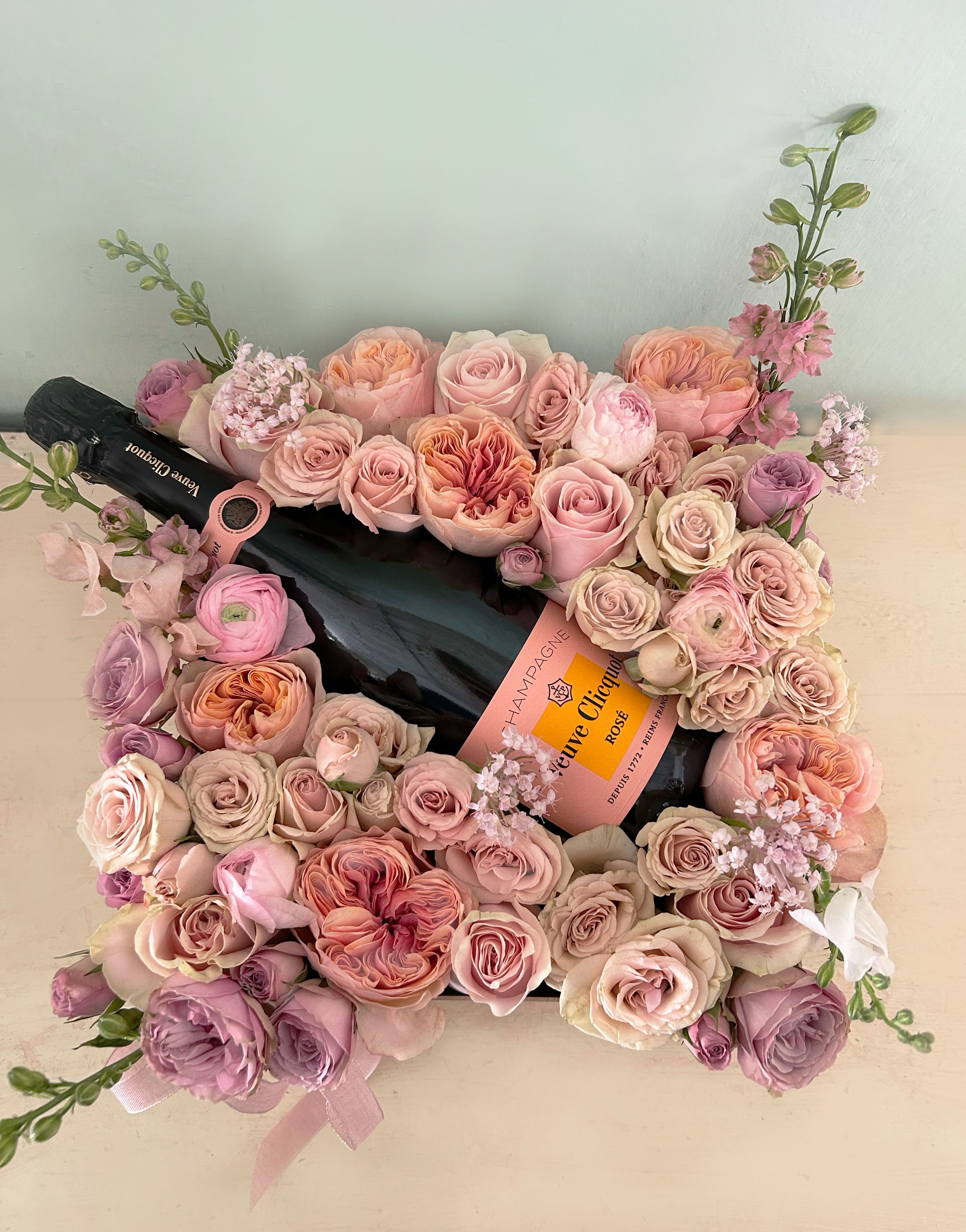 Champagne Rose Box - The ultimate luxury flower box to celebrate and cheer. A luxurious Veuve Cliquot Rose Champagne layed on a bed of gorgeous blushing roses and details of seasonal dreamy stems, all arranged in a reusable papermache  with beautiful ribbon. It's hard to find something more pretty and romantic.