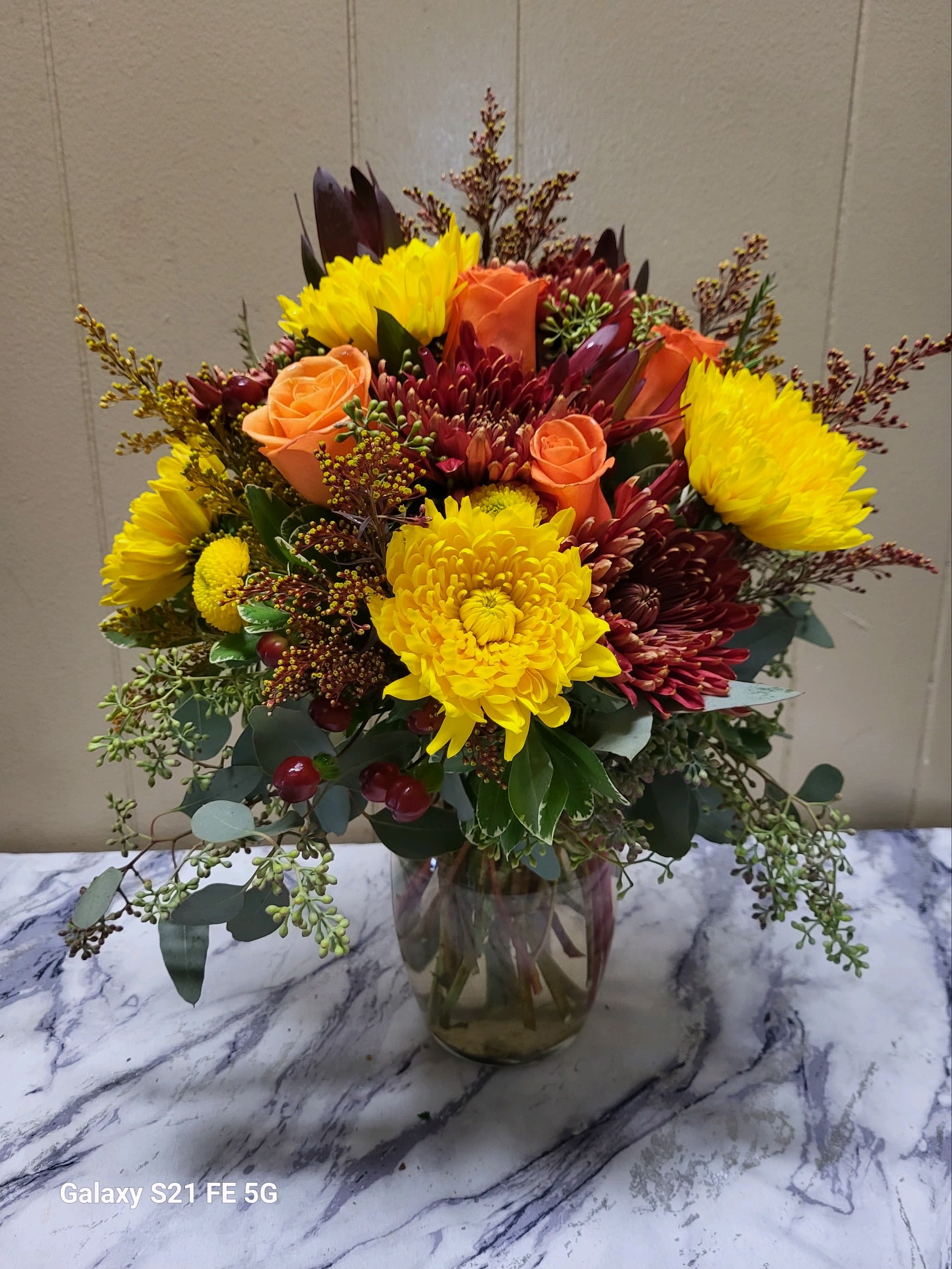 Mixed bouquet of yellow chrysanthemums and orange roses in a glass vase