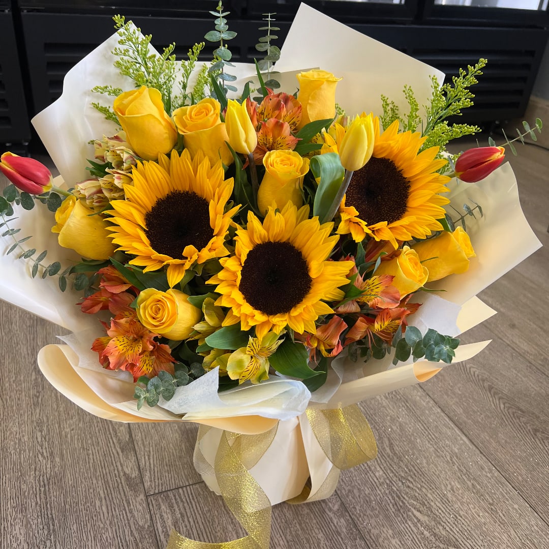 Bouquet of yellow roses and sunflowers with red tulips in cream wrap