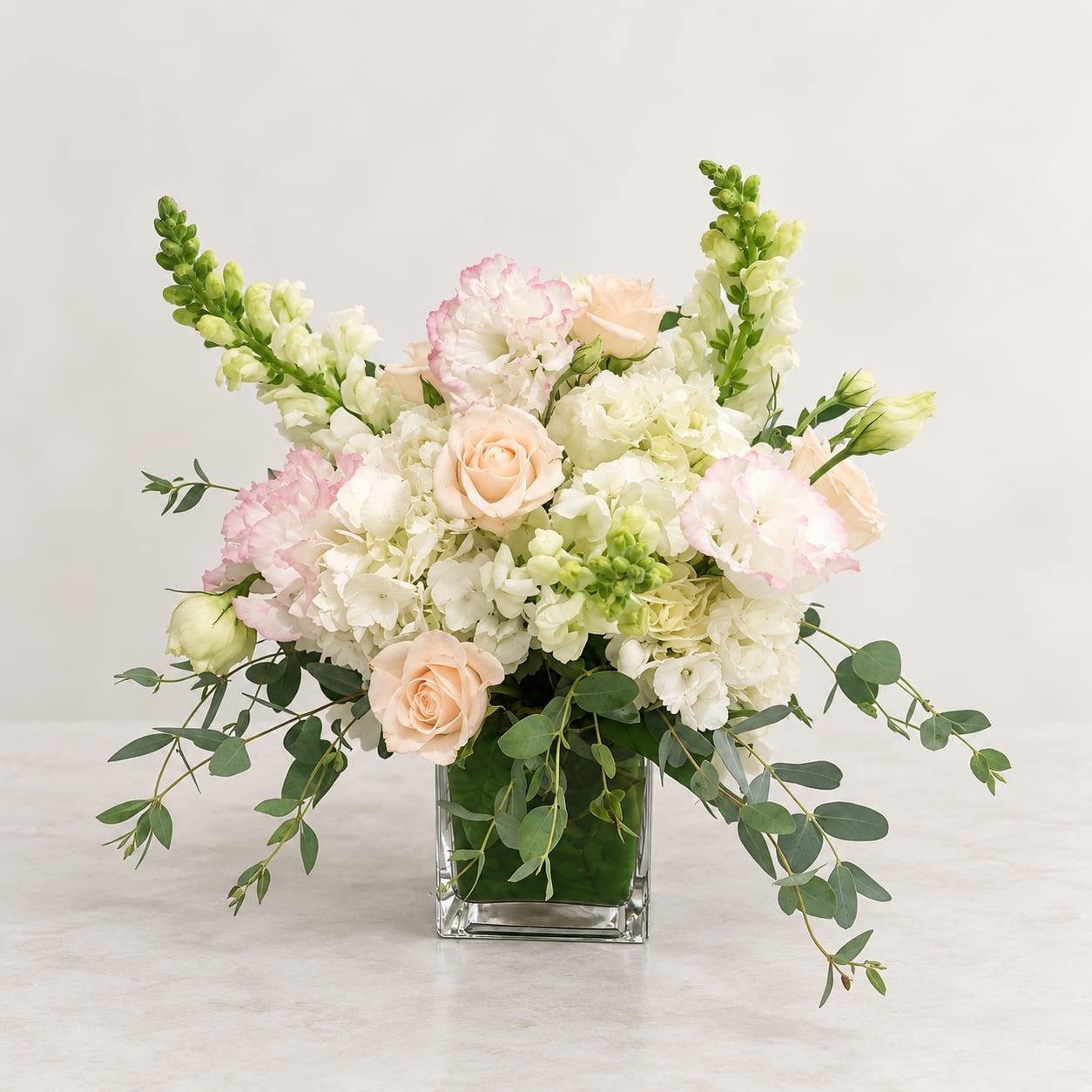 Wedding bouquet in a square glass vase with blush roses and white blooms