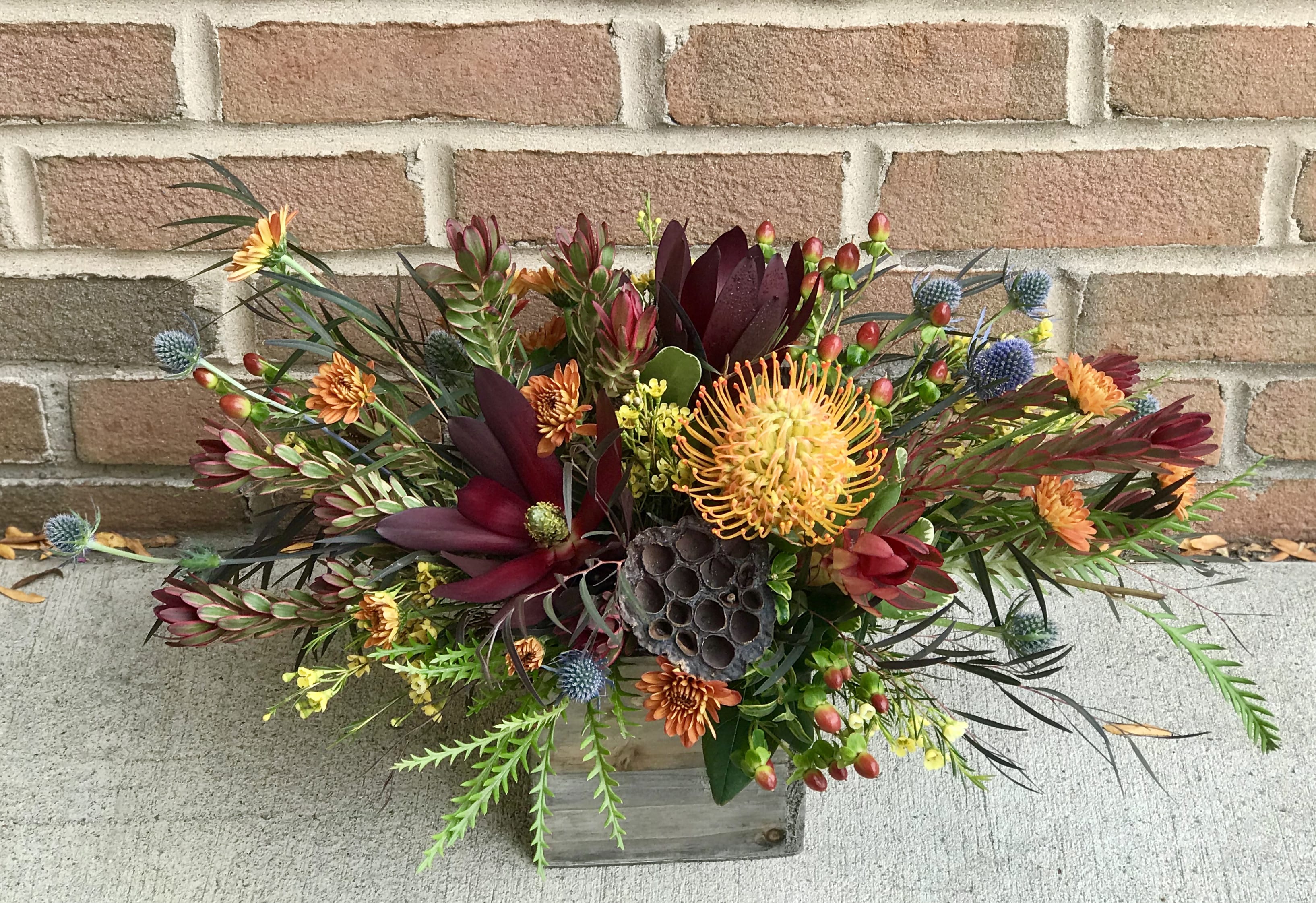 Mixed floral arrangement in a wooden box with orange and burgundy blooms