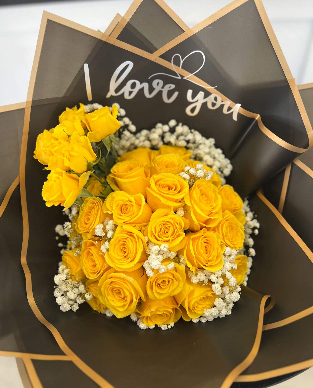 Bouquet of yellow roses with white filler flowers in black wrap