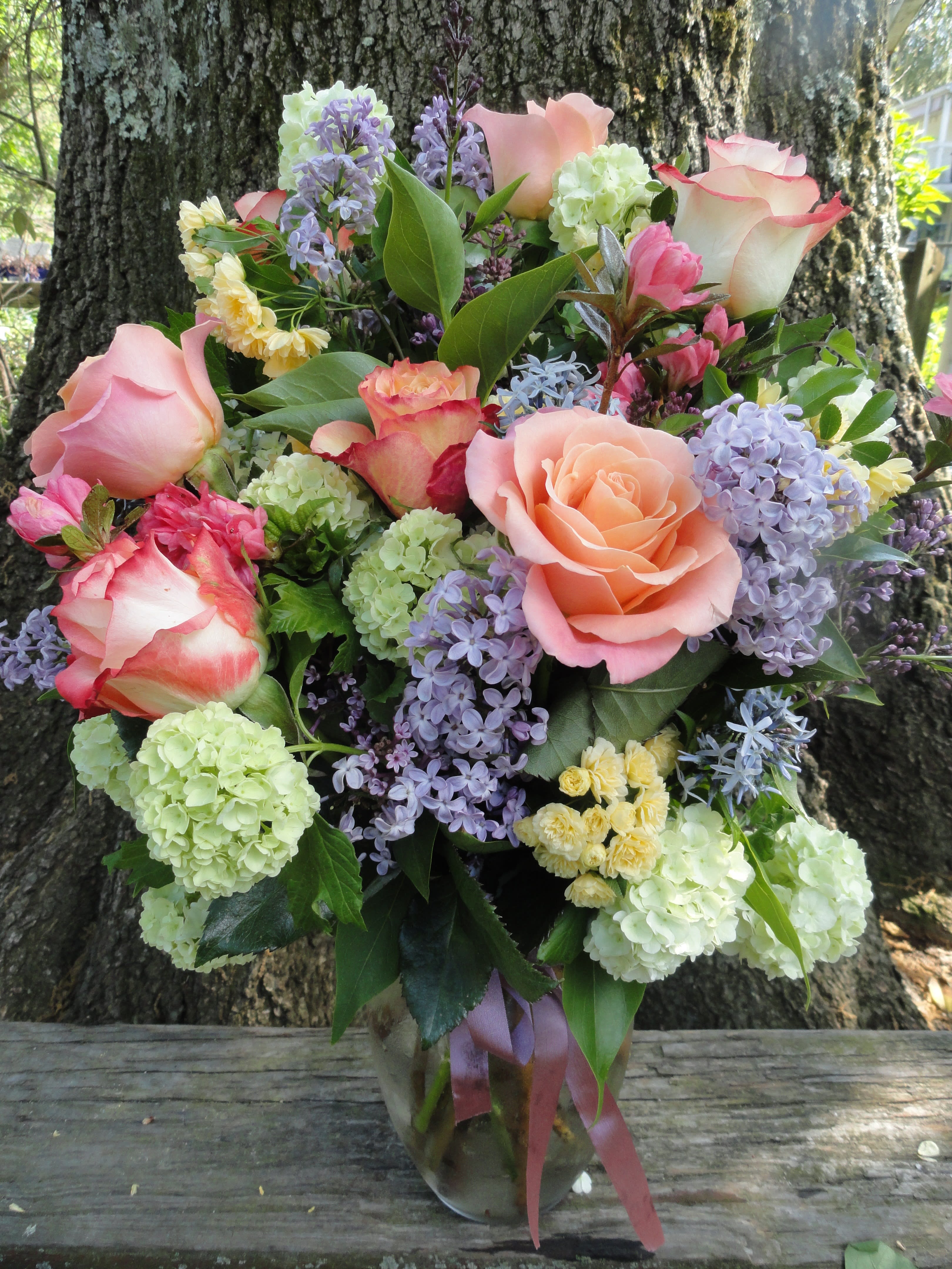 Bouquet of pink roses, lilac blooms, and pale green hydrangeas in a glass vase