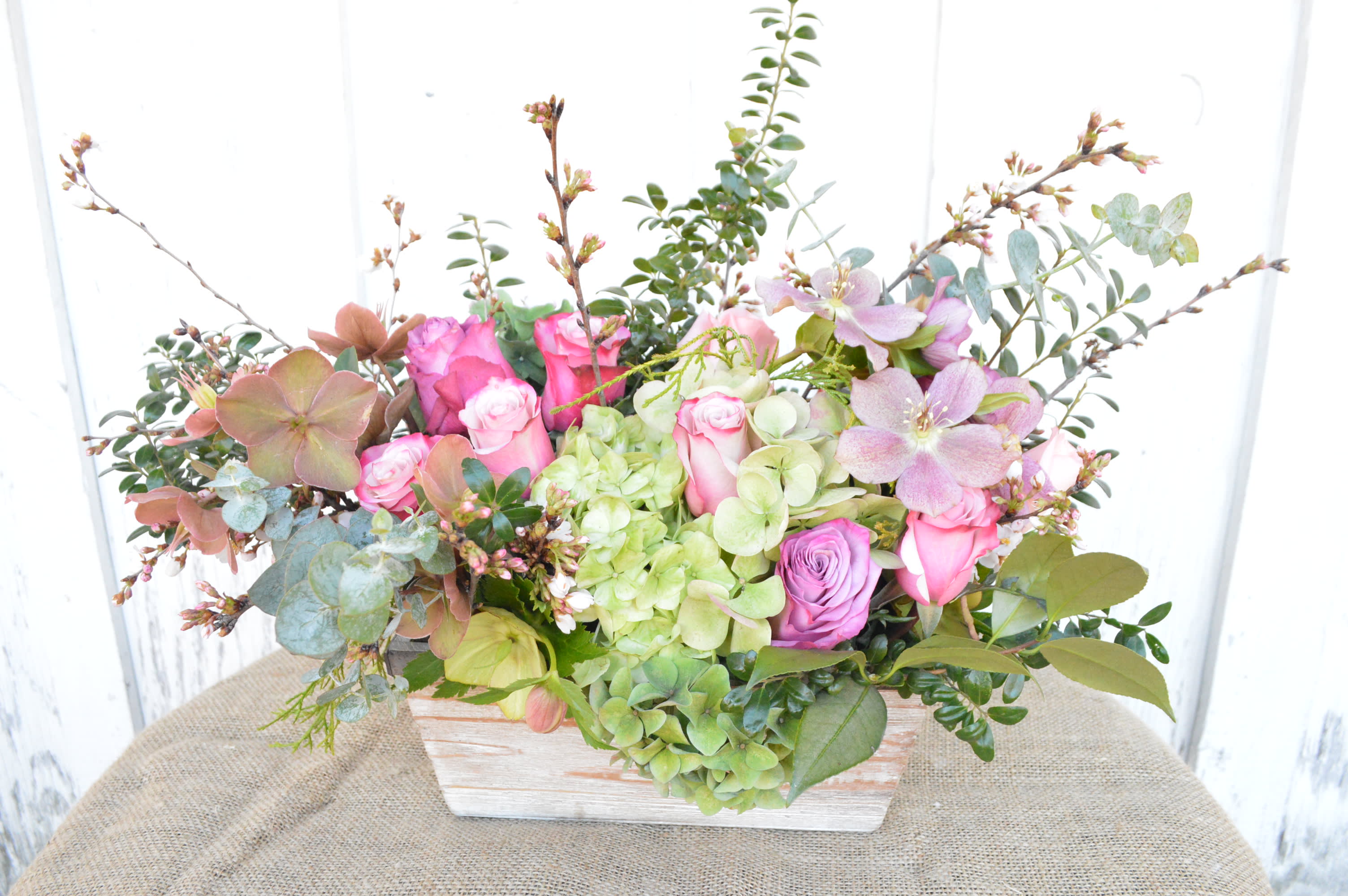 Pink roses and green hydrangeas in a white wooden box with eucalyptus