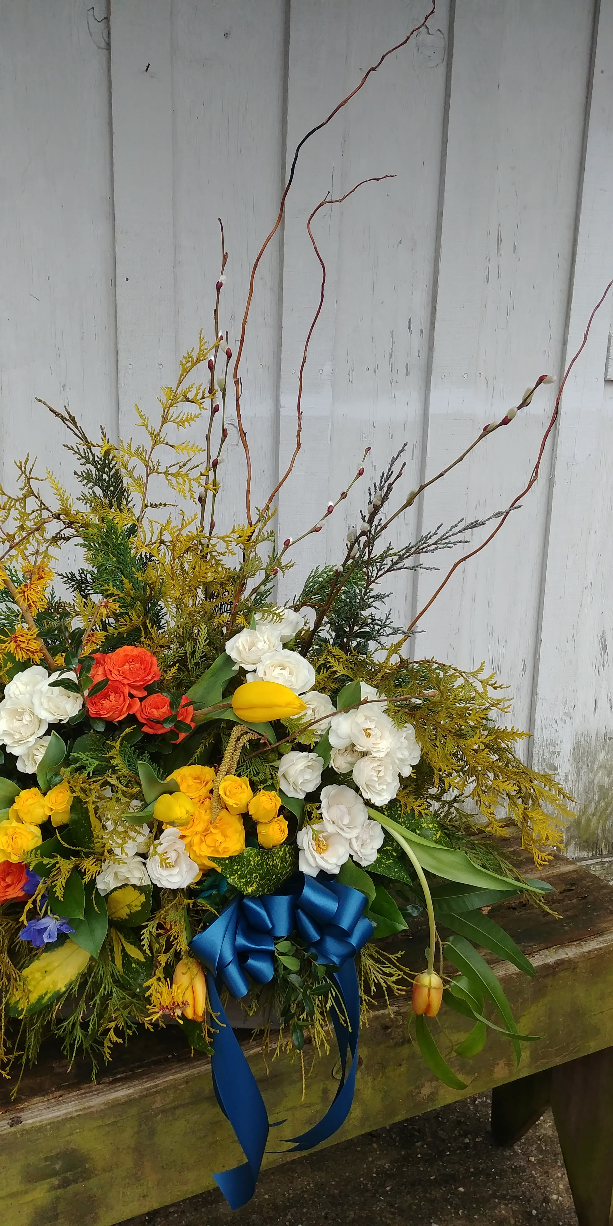 Large mixed floral arrangement with white, yellow, and orange blooms and a blue ribbon