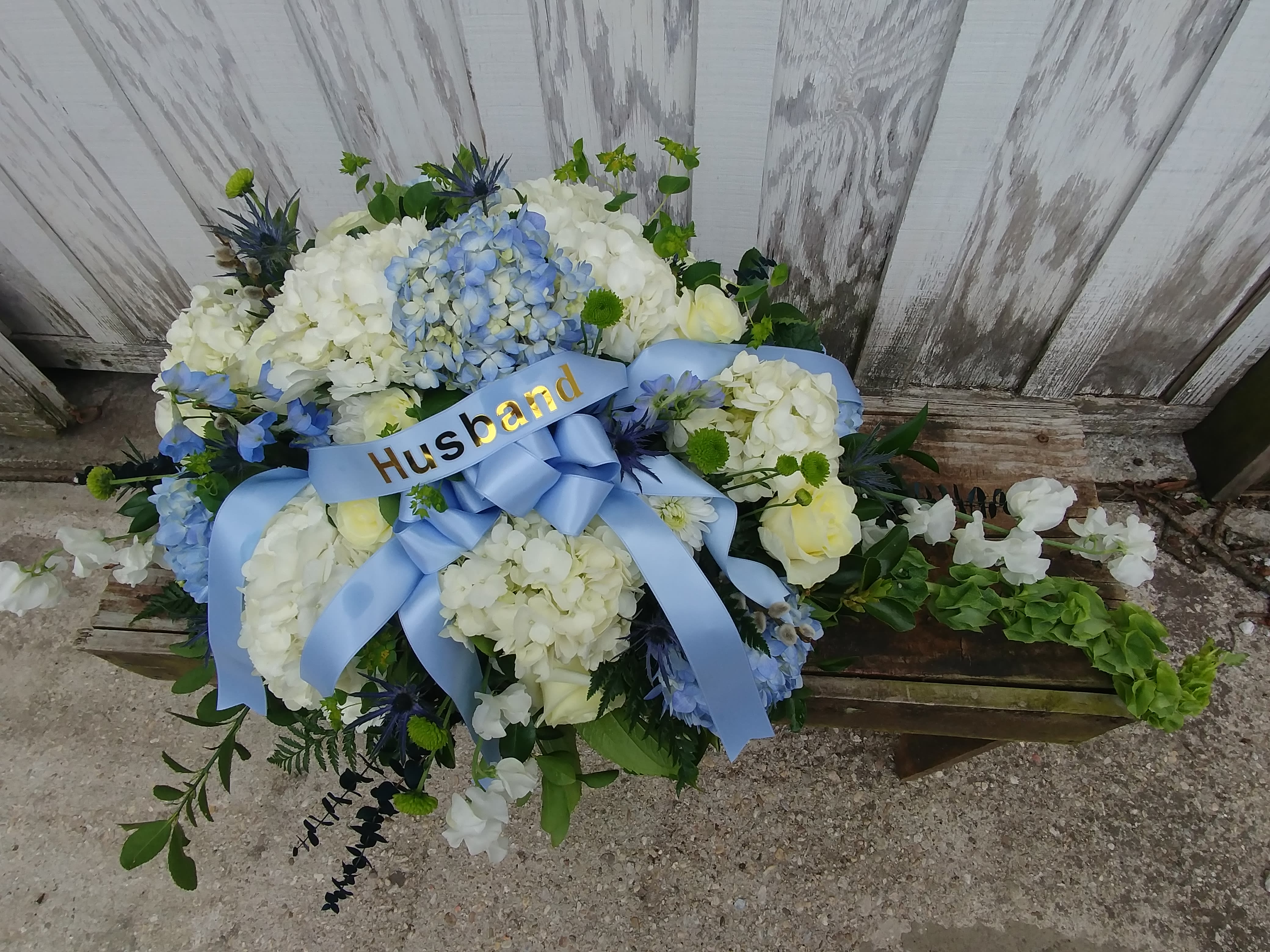 White and blue floral arrangement with a blue ribbon labeled Husband