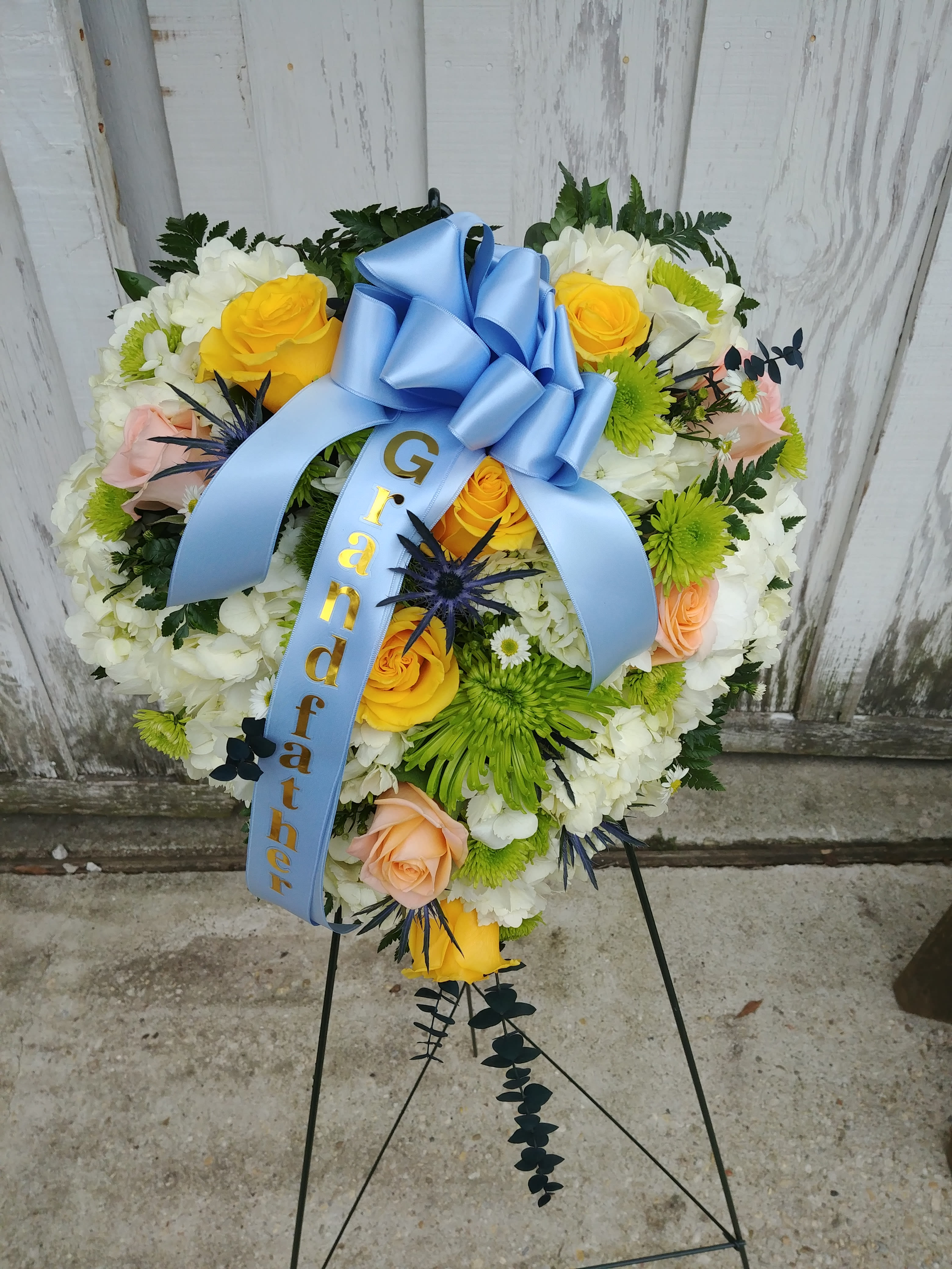 Heart-shaped floral wreath with a blue ribbon and stand