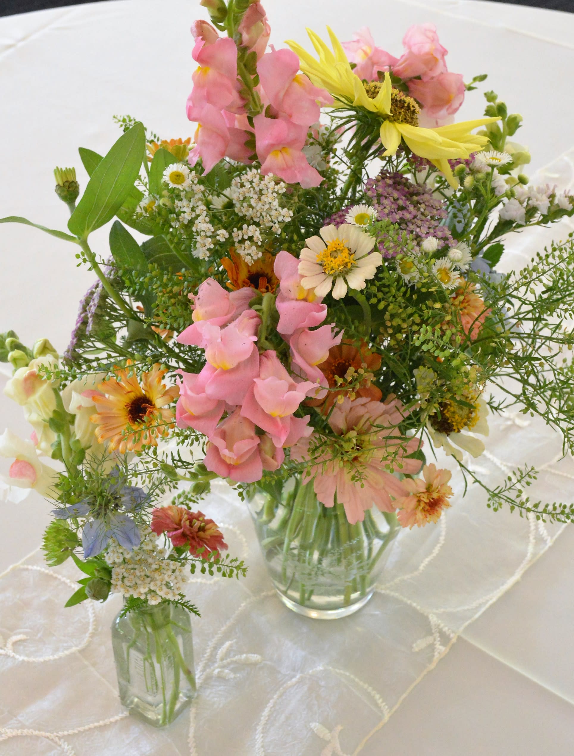 Mixed pastel flower arrangements in clear glass vases on a white tablecloth