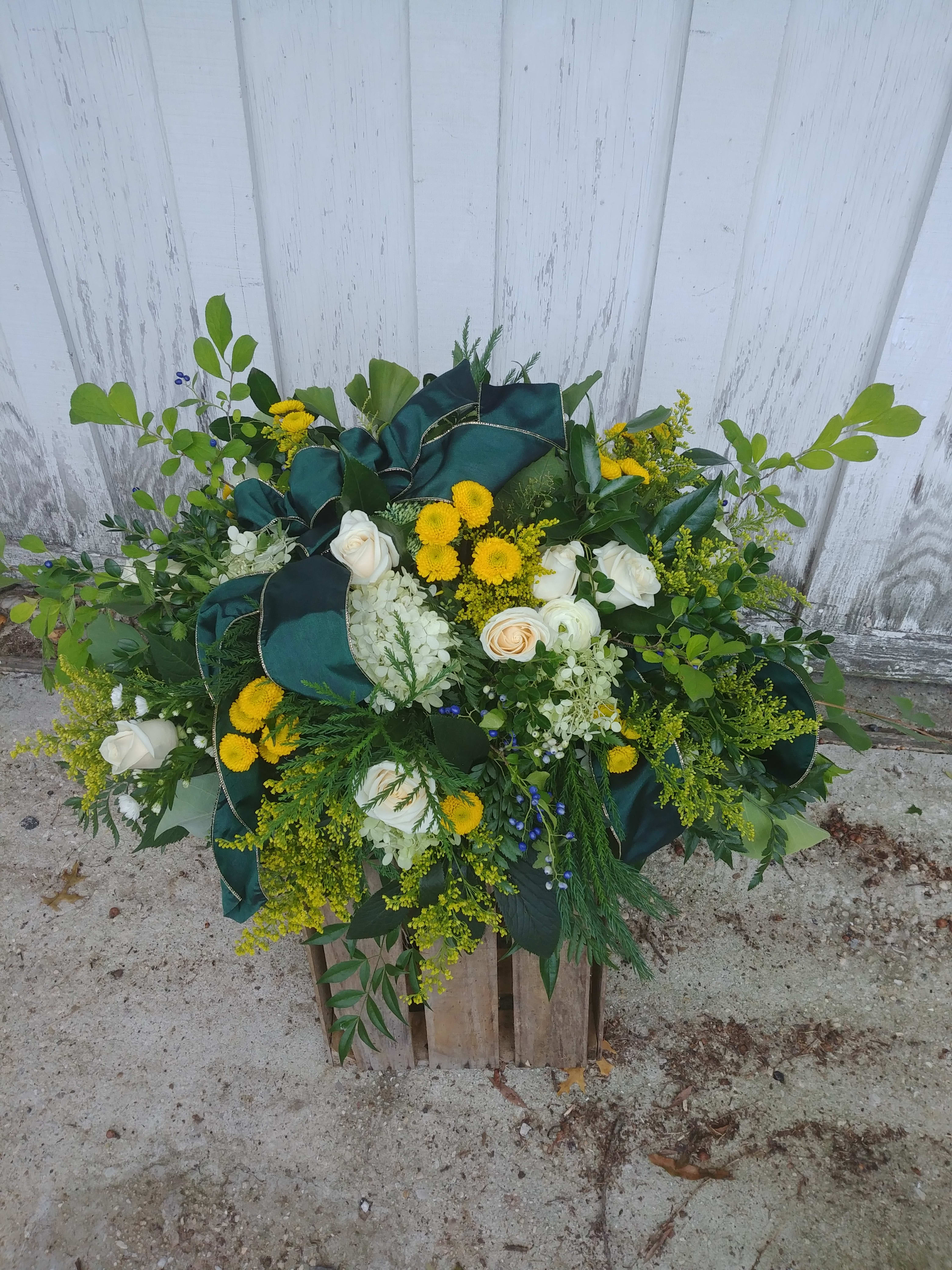 Large floral arrangement with white roses, yellow blooms, and dark green ribbon