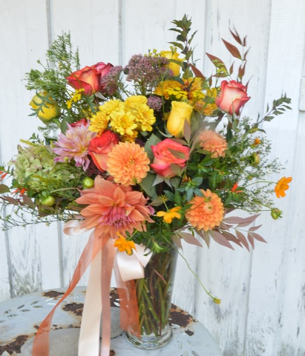 Mixed bouquet of roses, dahlias, and yellow blooms in a glass vase