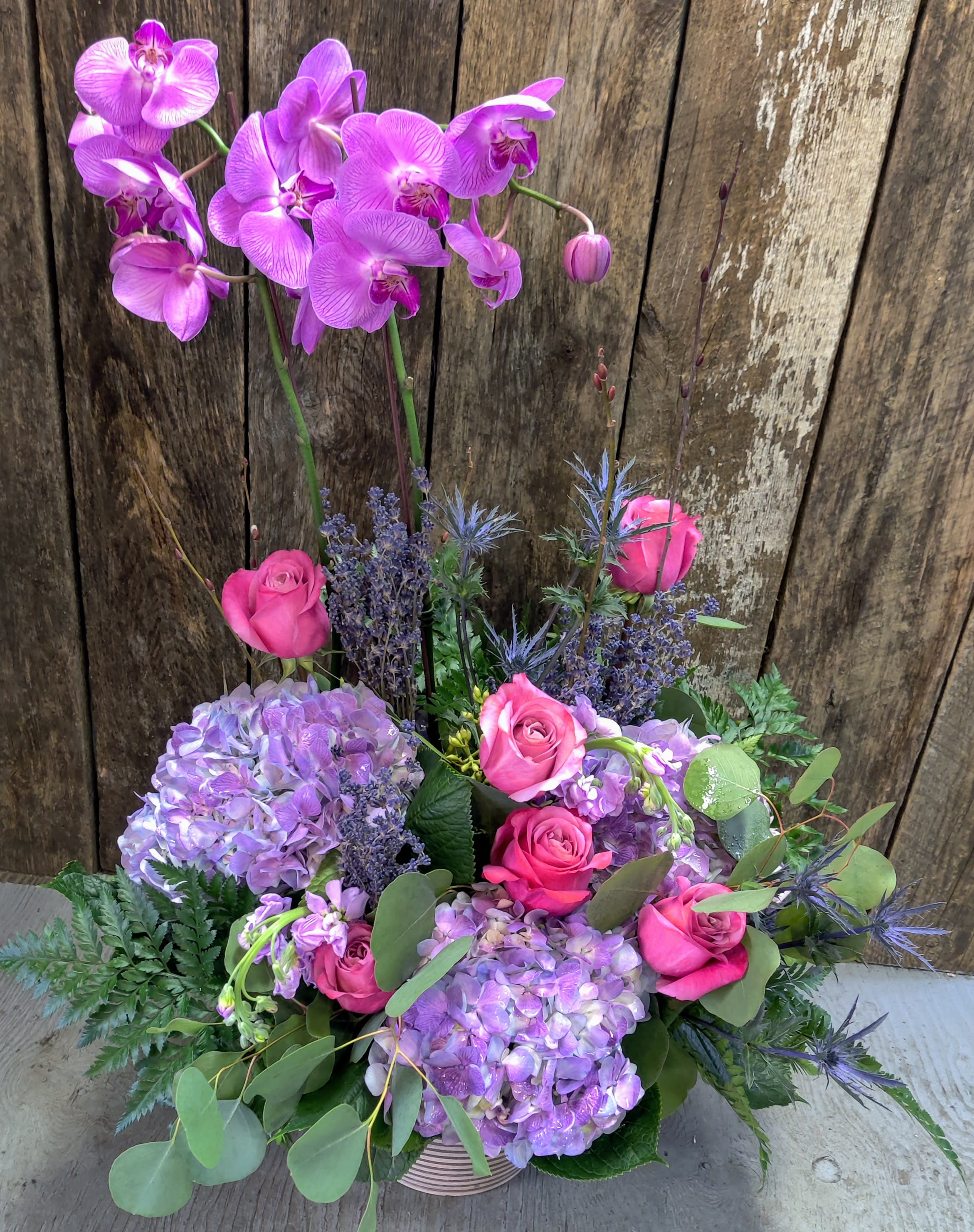Pink orchids and roses arranged with lavender hydrangeas in a basket