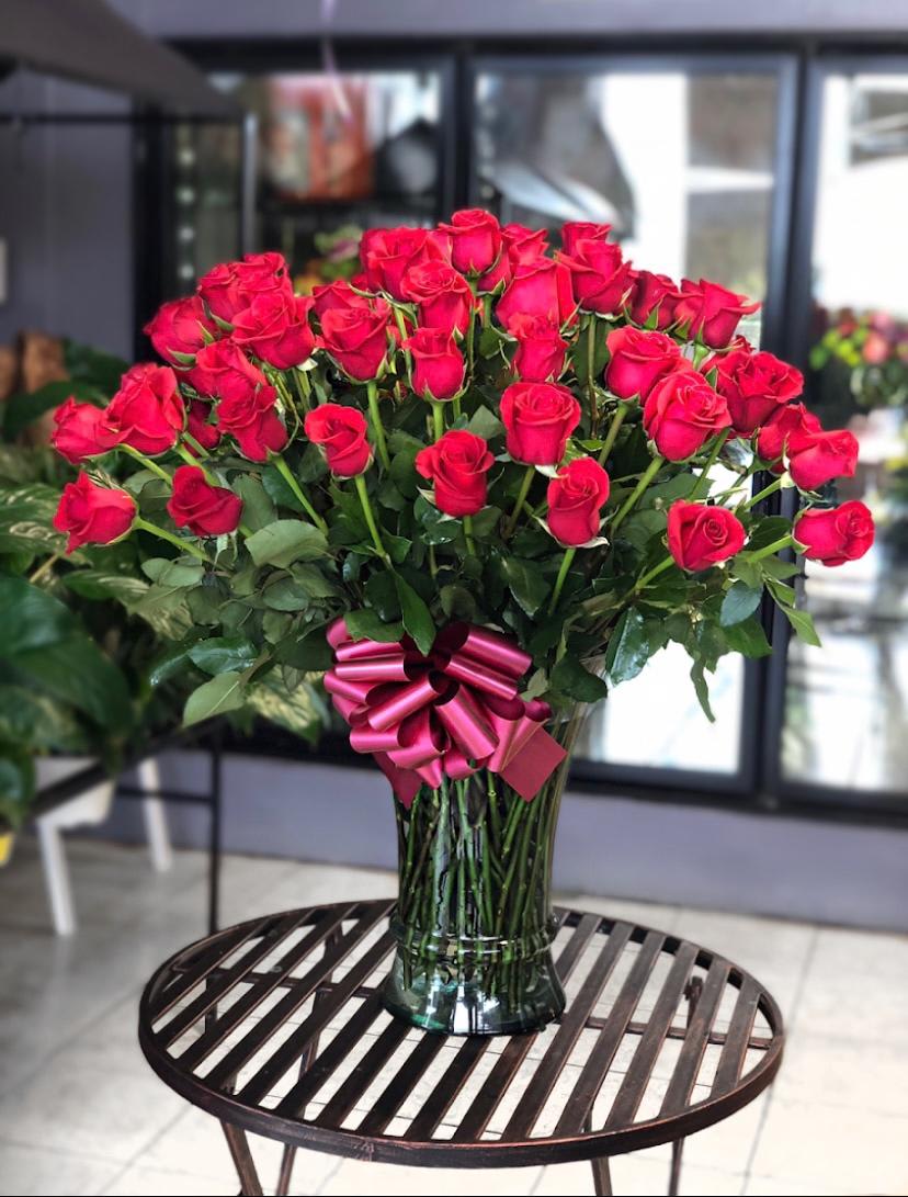 Large bouquet of red roses in a glass vase with a pink ribbon