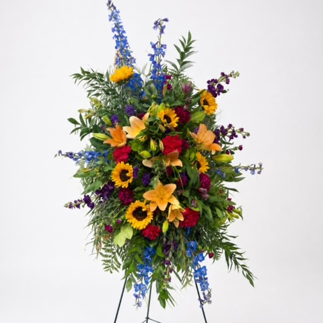 Tall standing floral spray with sunflowers, lilies, and blue flowers
