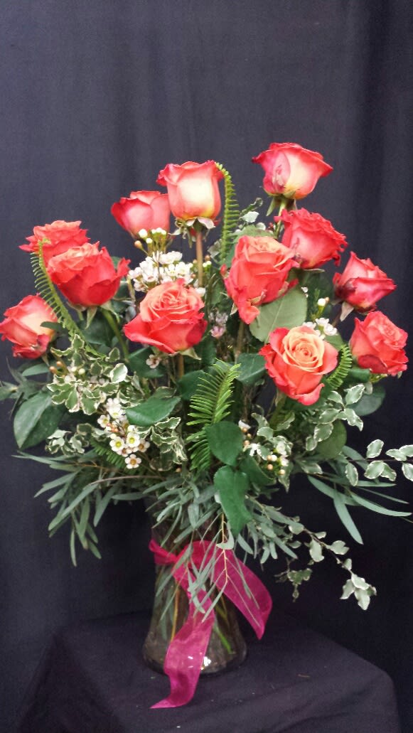 Red roses arranged in a glass vase with greenery and a pink ribbon