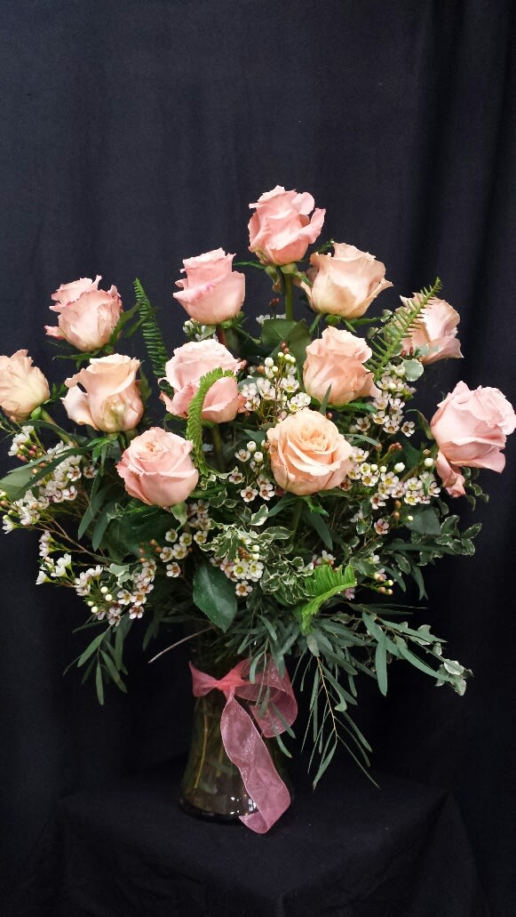 Pink roses arranged in a glass vase with a pink ribbon