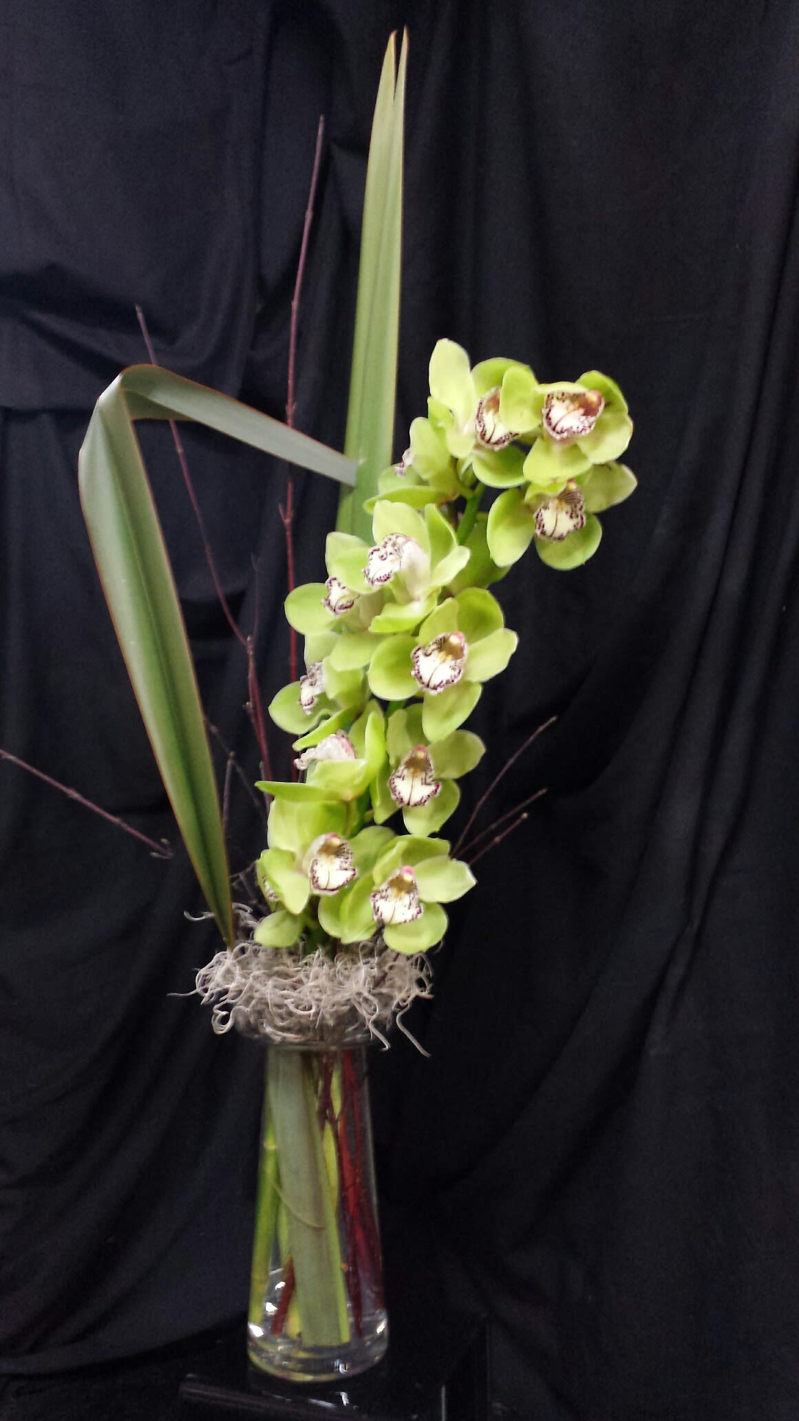 Green orchid arrangement in a tall glass vase with long leaves