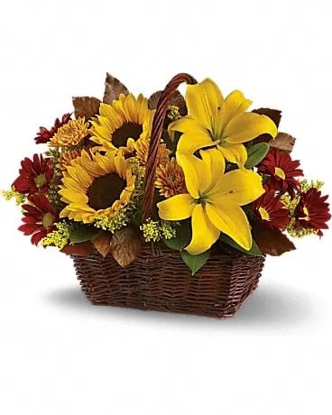 Basket arrangement with yellow lilies, sunflowers, and red mums in a brown wicker basket