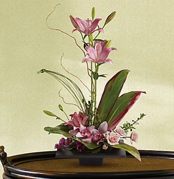 Imagination Blooms with Cymbidium Orchids - This towering topiary of asiatic lilies, orchids and roses - artistically arranged with tropical greenery - is a unique gift that celebrates the spirit of creativity. Pink asiatic lilies rise up from a square design block holding a mix of cymbidium orchids, spray roses and accent blooms and greenery. 