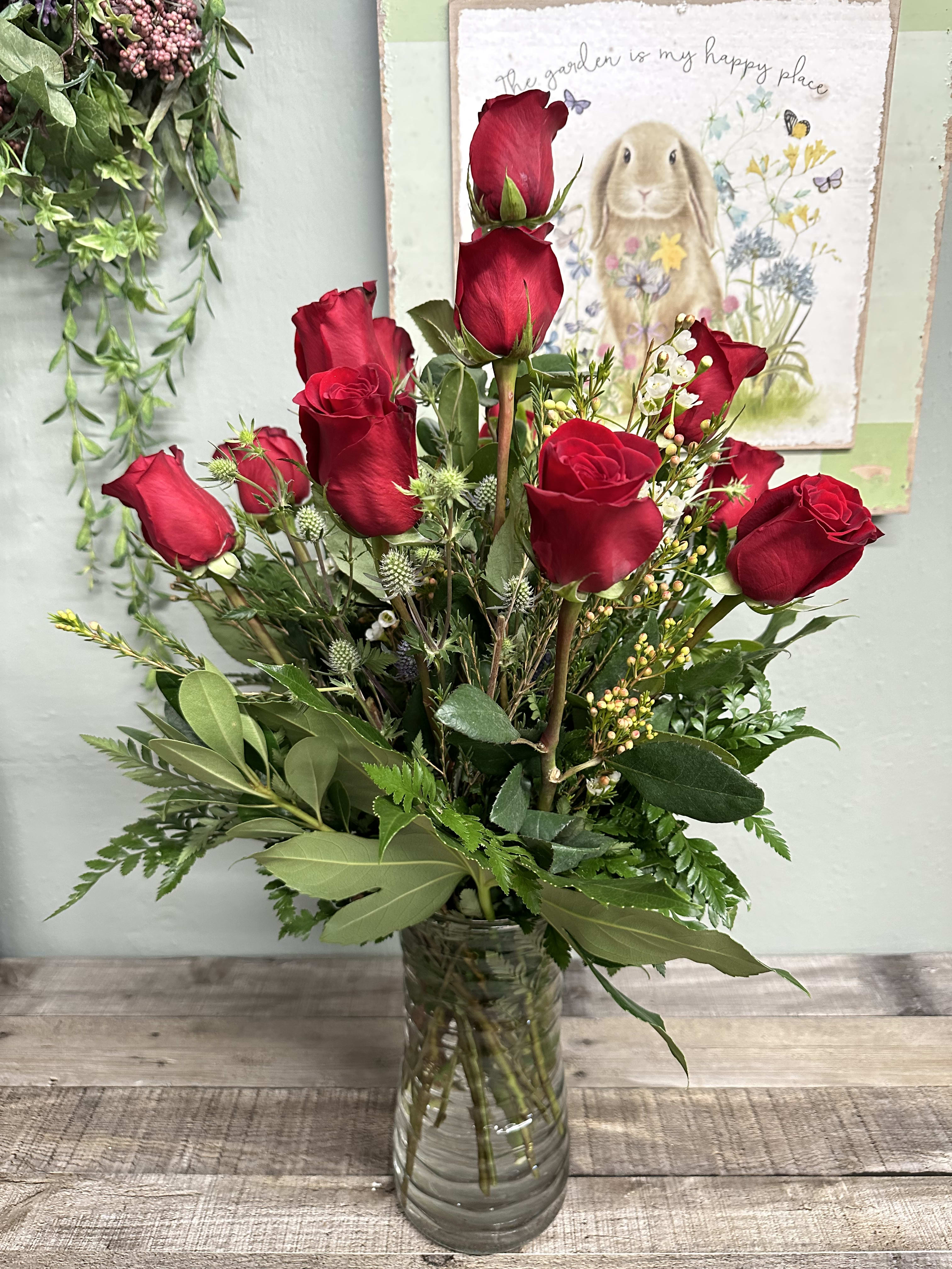 Red roses arranged in a clear glass vase with mixed greenery