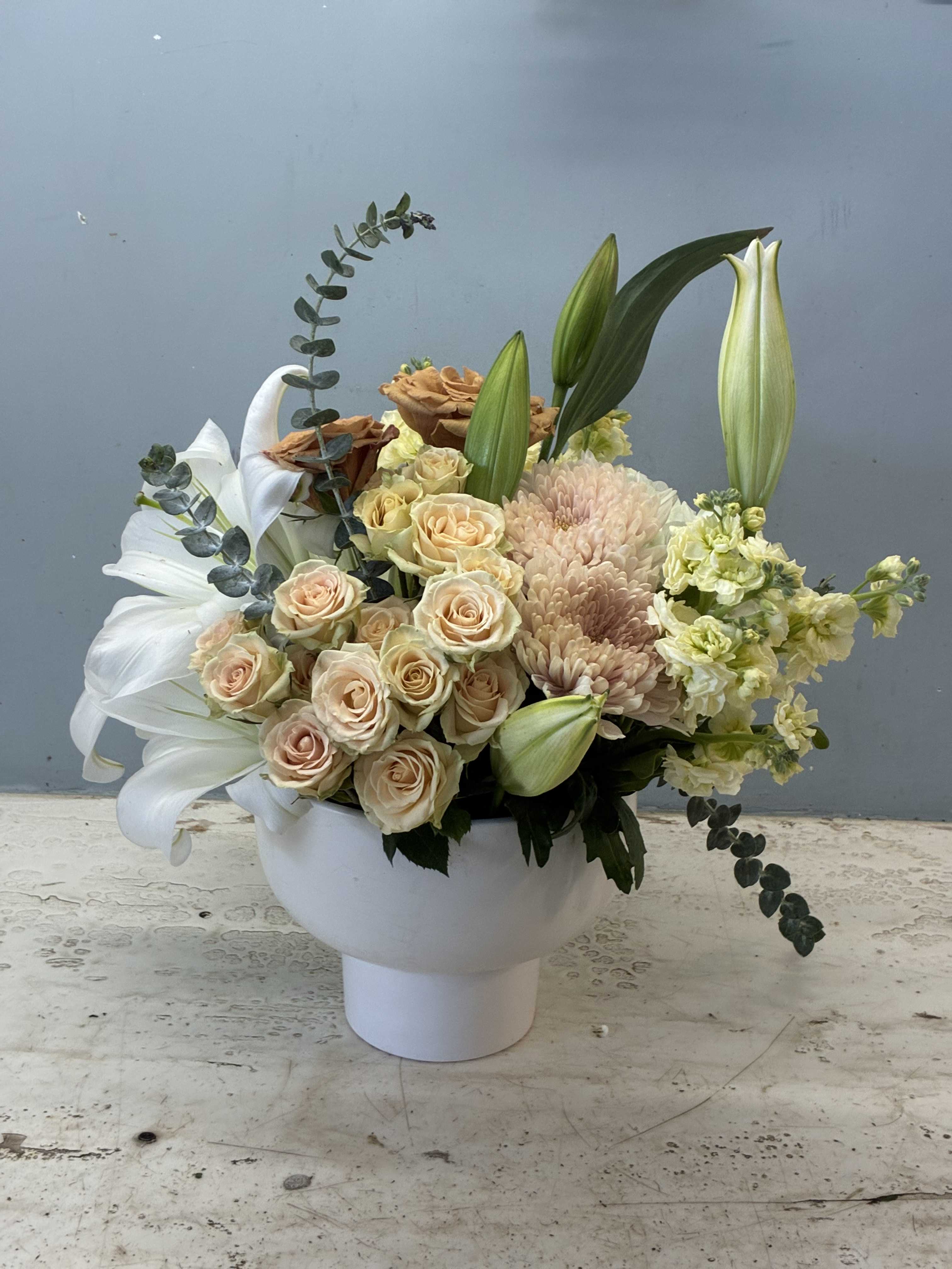 Cream roses and lilies arranged in a white pedestal vase