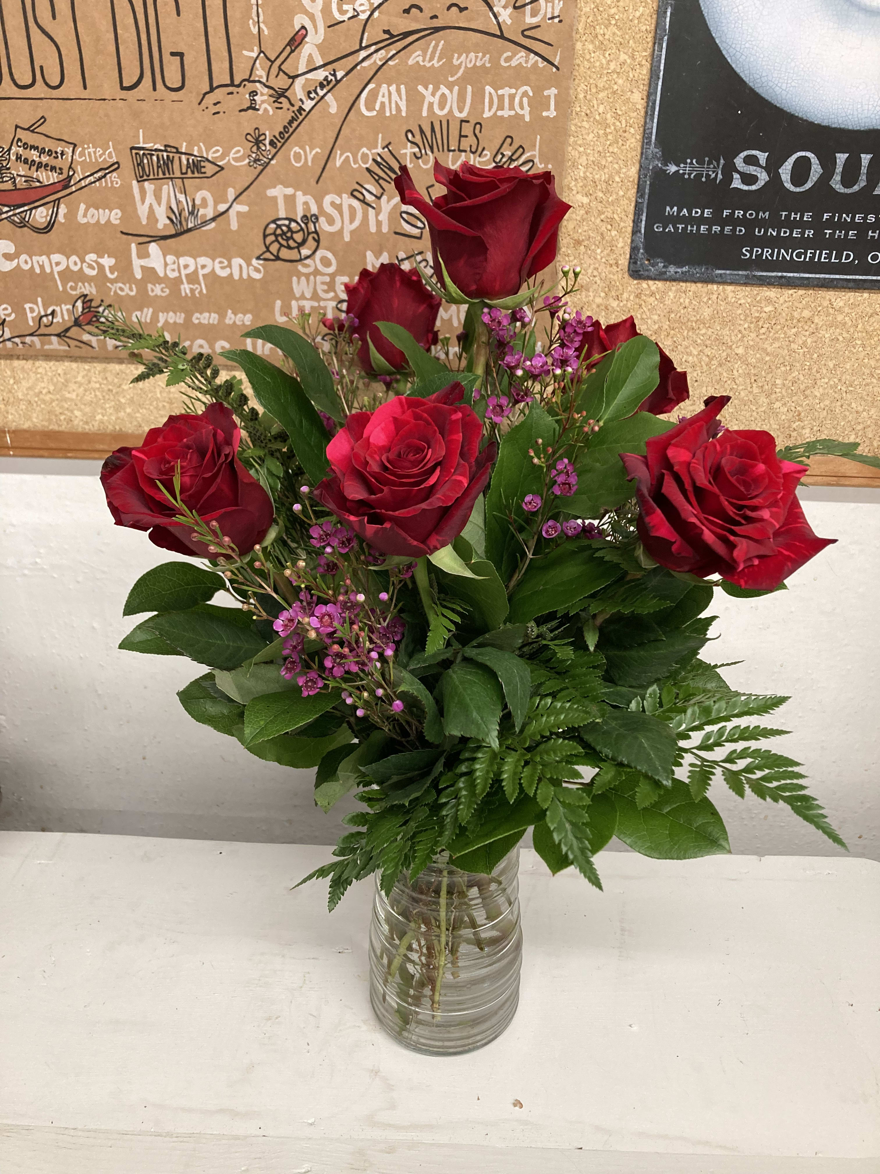 Red roses arranged in a clear glass vase with small purple filler flowers