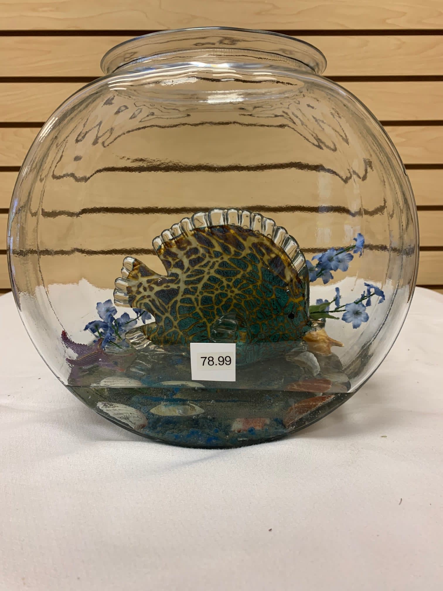 Glass fish bowl with a decorative fish and small blue flowers inside