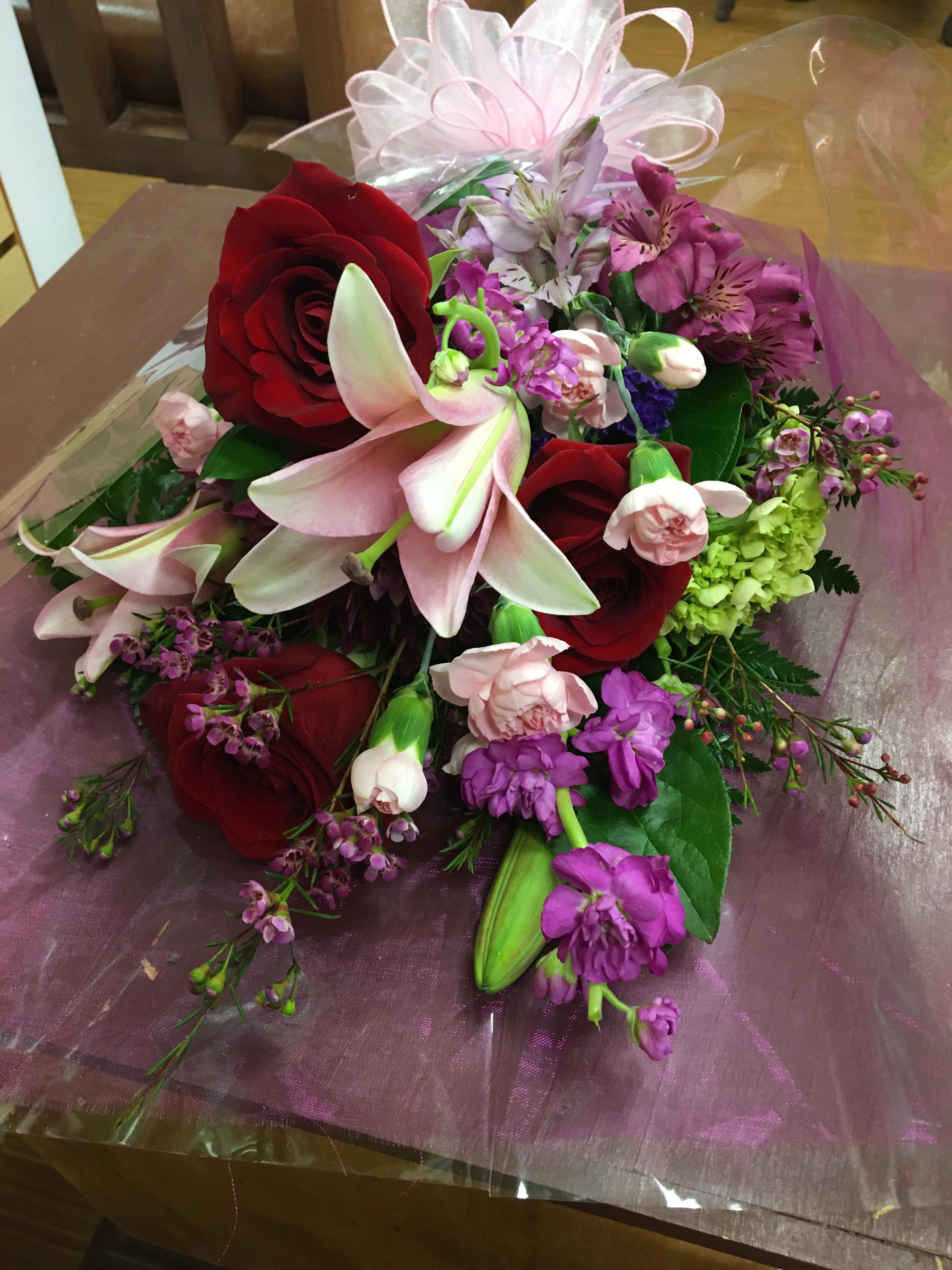 Bouquet of red roses, pink lilies, and purple flowers wrapped in clear cellophane