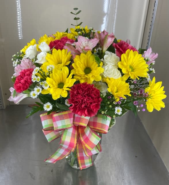 Mixed bouquet of yellow daisies, pink carnations, and white roses in a glass vase
