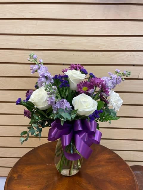 Bouquet of white roses and purple flowers in a glass vase with a purple ribbon