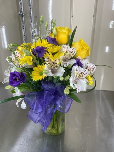 Bouquet of yellow roses, purple lisianthus, and white alstroemeria in a glass vase