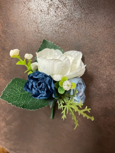 Small blue and white floral boutonniere with green leaves
