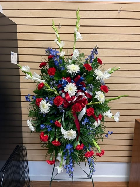 Standing floral spray with red, white, and blue flowers on a metal easel