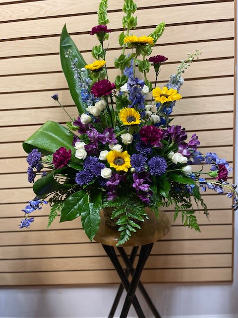 Tall mixed flower arrangement in a bronze vase with yellow, purple, blue, and white blooms