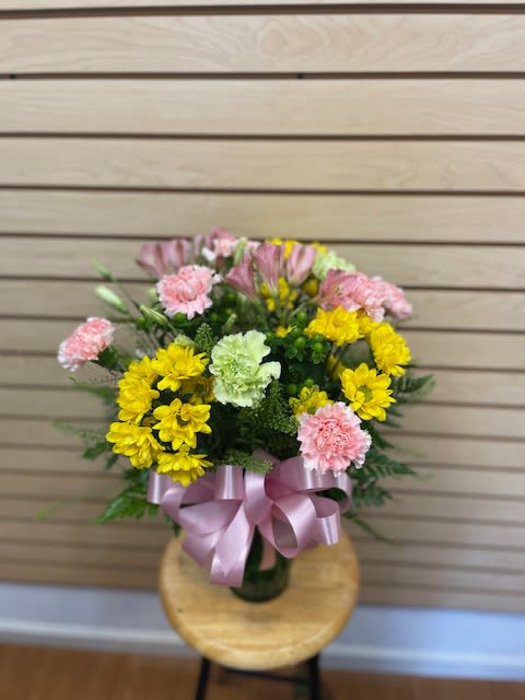 Bouquet of yellow and pink flowers tied with a pink ribbon in a vase