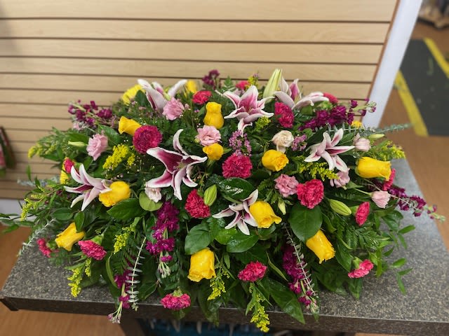 Large mixed floral arrangement with yellow roses, pink carnations, and lilies