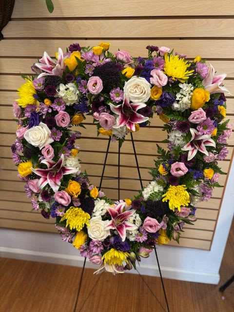 Heart-shaped floral wreath on a stand with pink, white, yellow, and purple flowers