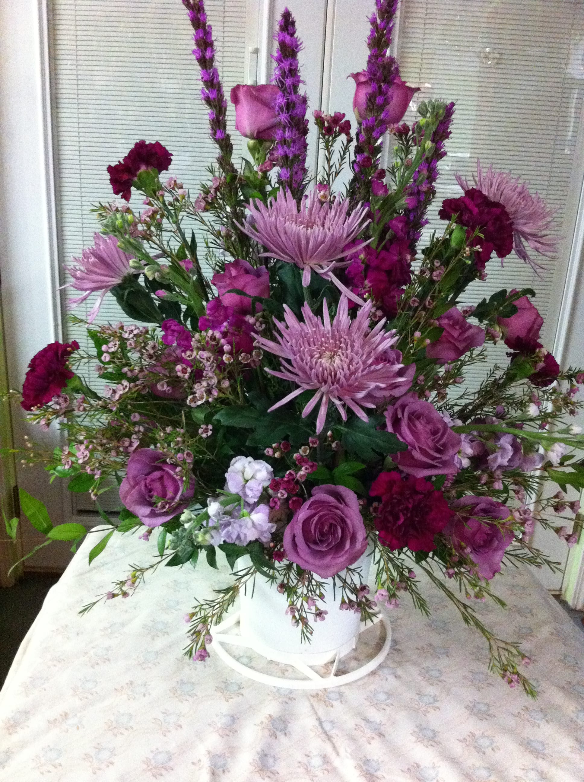 Purple floral arrangement in a white container with roses and tall blooms