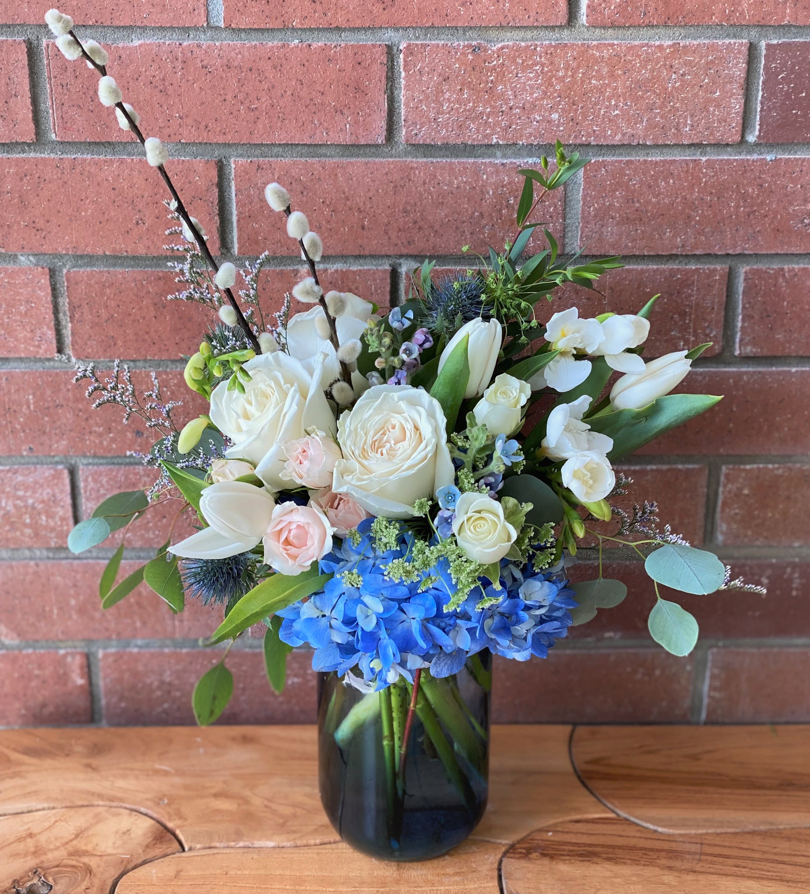 Vase arrangement of white roses, tulips, and blue hydrangeas with pussy willow branches