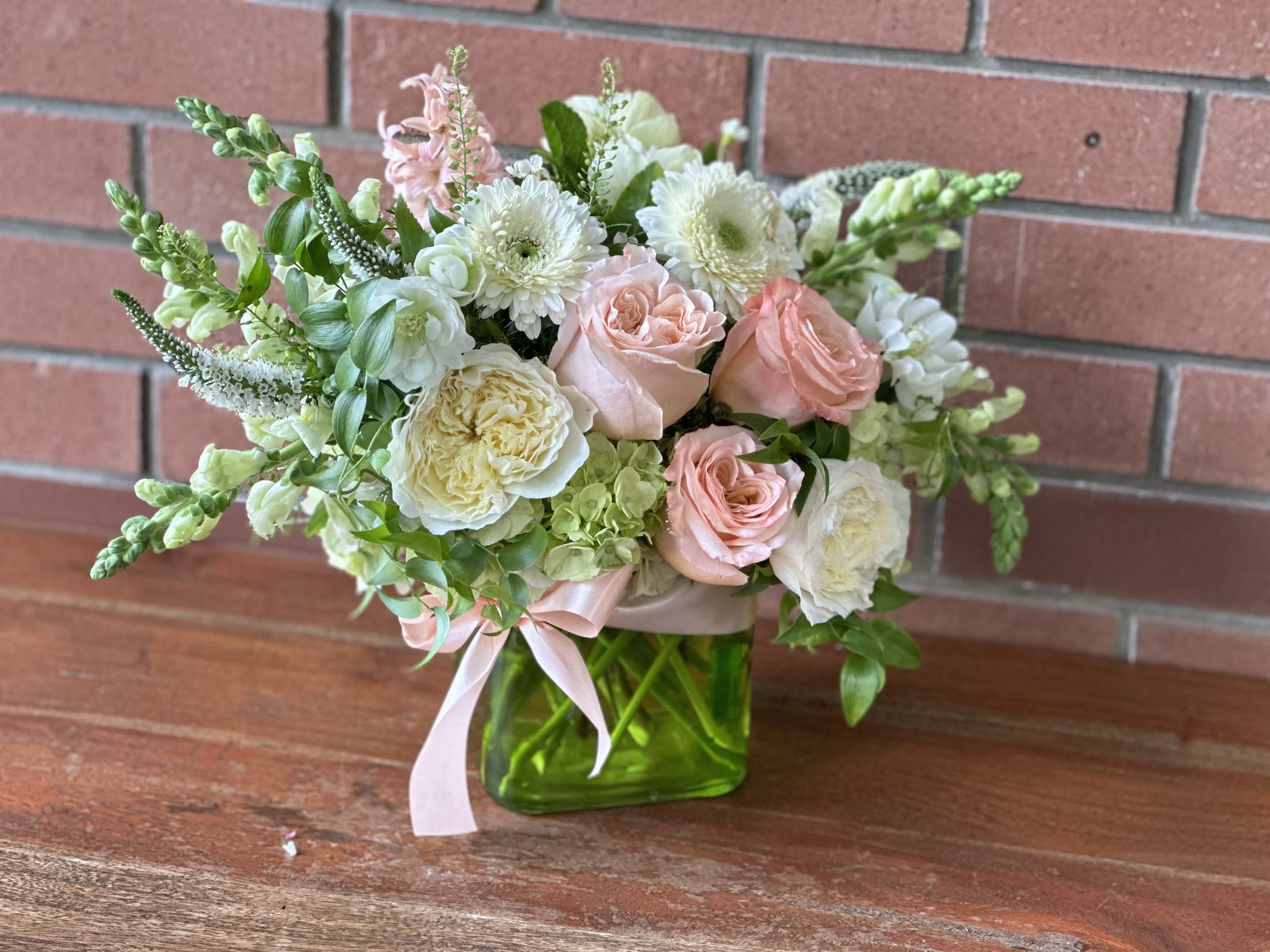 Compact arrangement of blush roses and white blooms in a green glass cube vase with pink ribbon