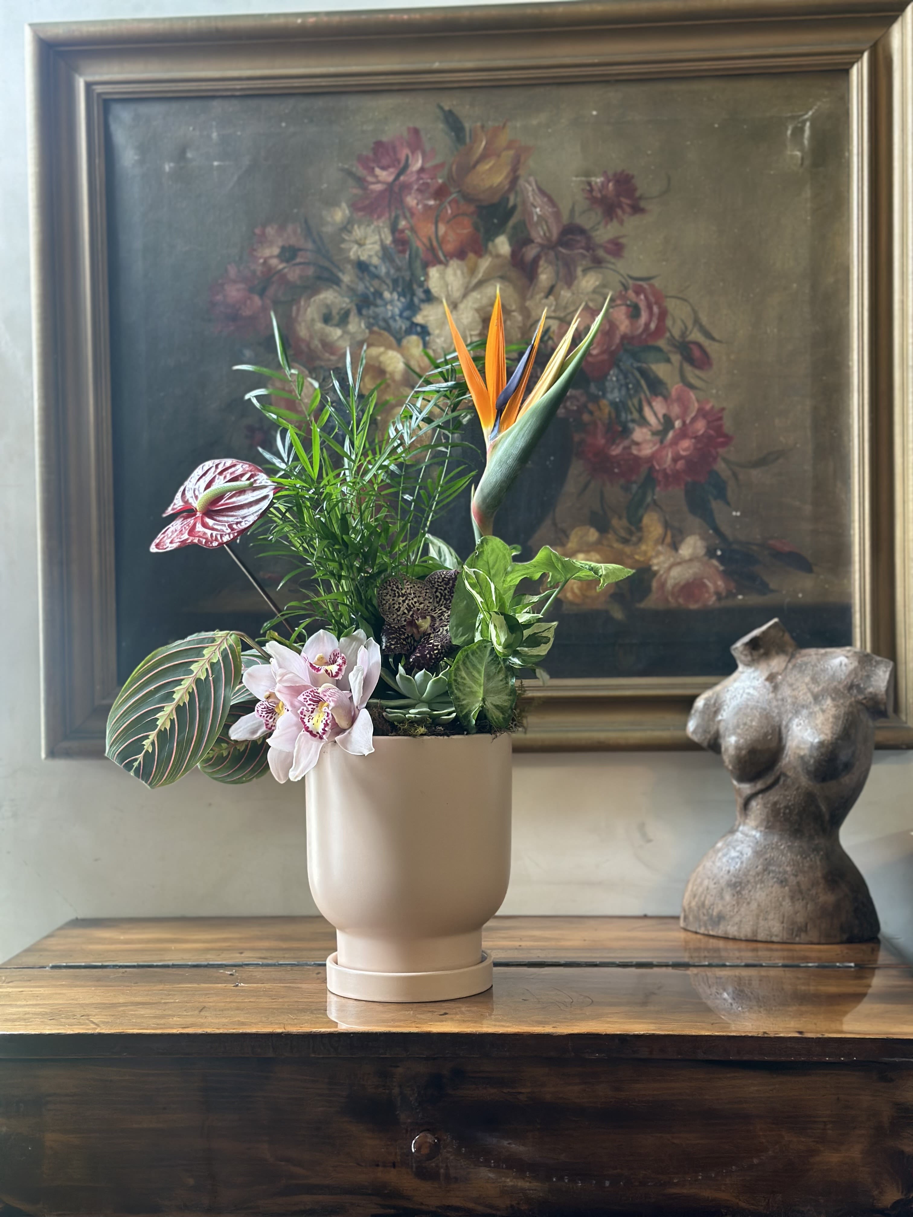 Tropical plant arrangement in a beige pot with bird of paradise and orchids