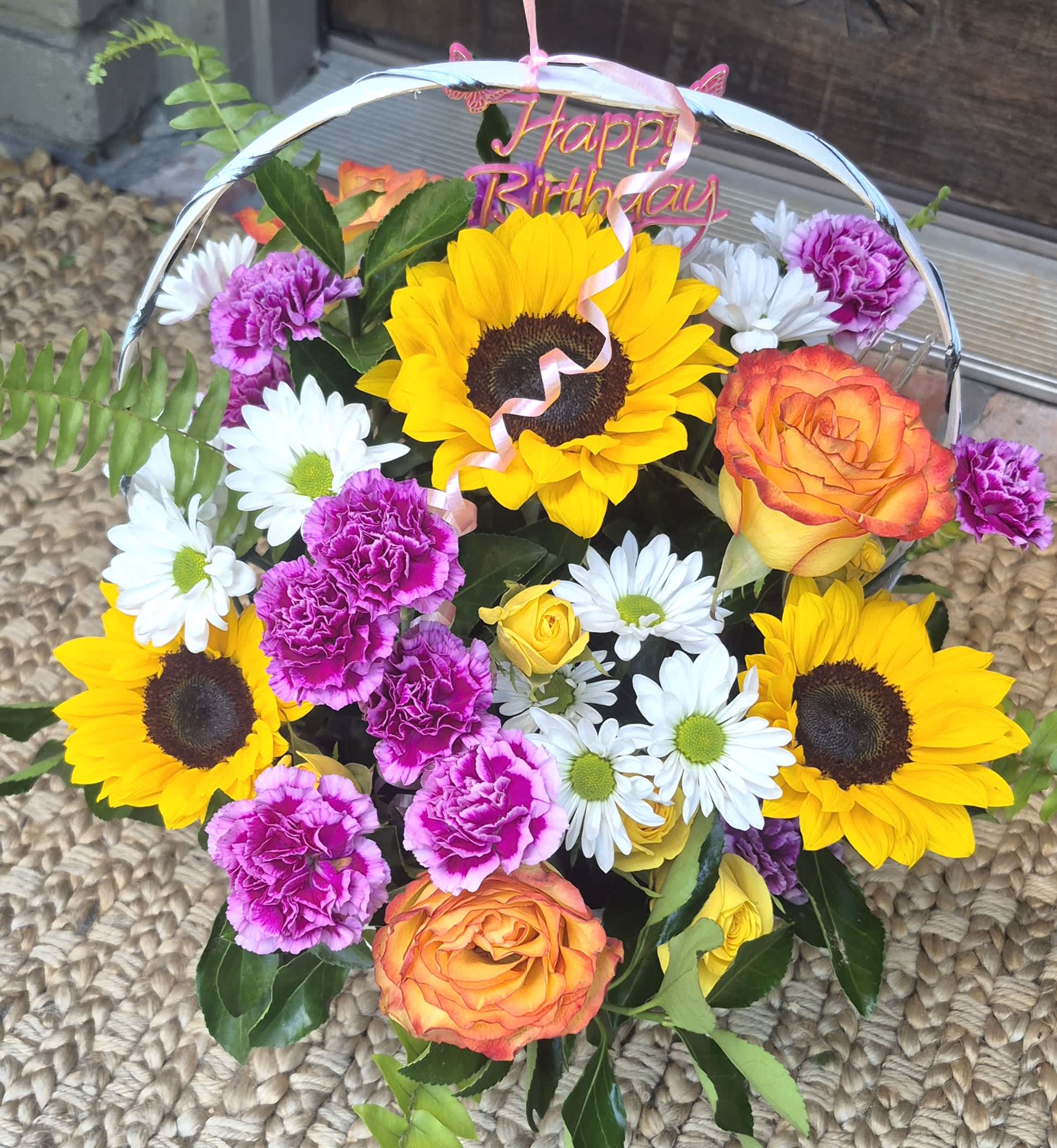 Mixed bouquet with sunflowers, roses, daisies, and carnations under a Happy Birthday topper
