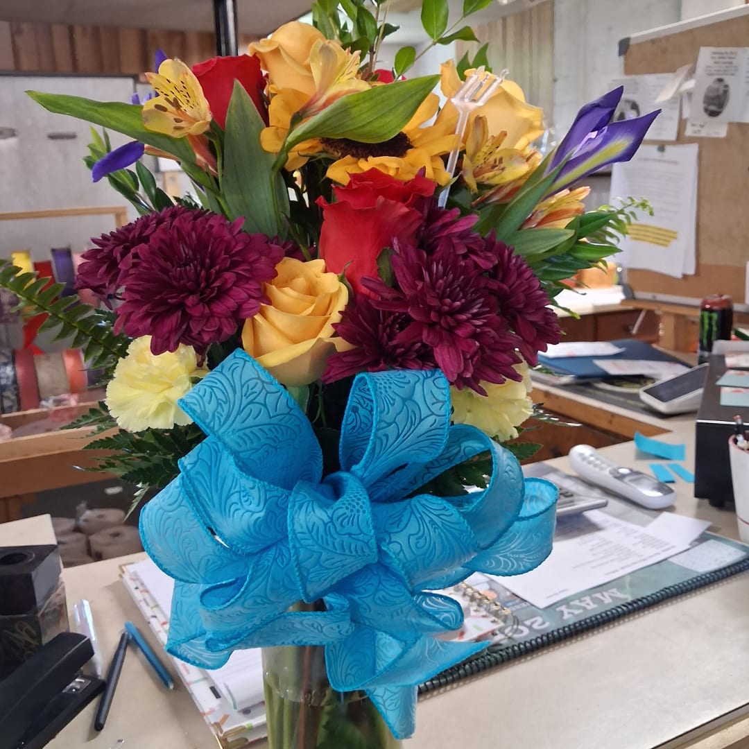 Mixed bouquet of roses, sunflowers, and chrysanthemums with a large blue ribbon