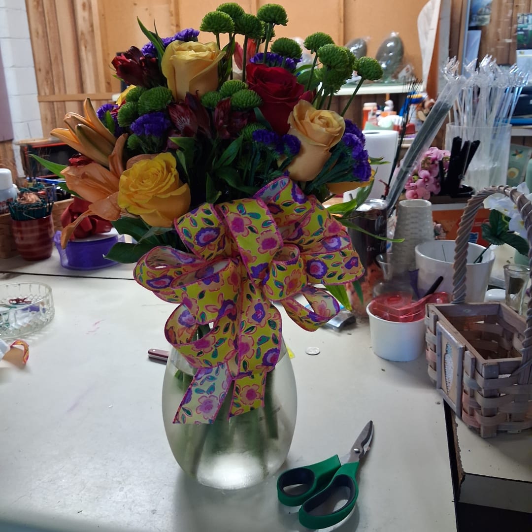 Mixed bouquet of roses and lilies in a glass vase with a patterned ribbon